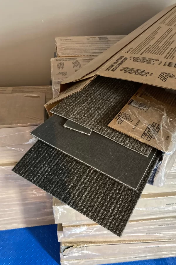 A stockpile of new carpet tiles awaiting installation in Chase Hall. Because of its long and narrow shape, this format is called a plank tile. (Doug Hubley/Bates College)