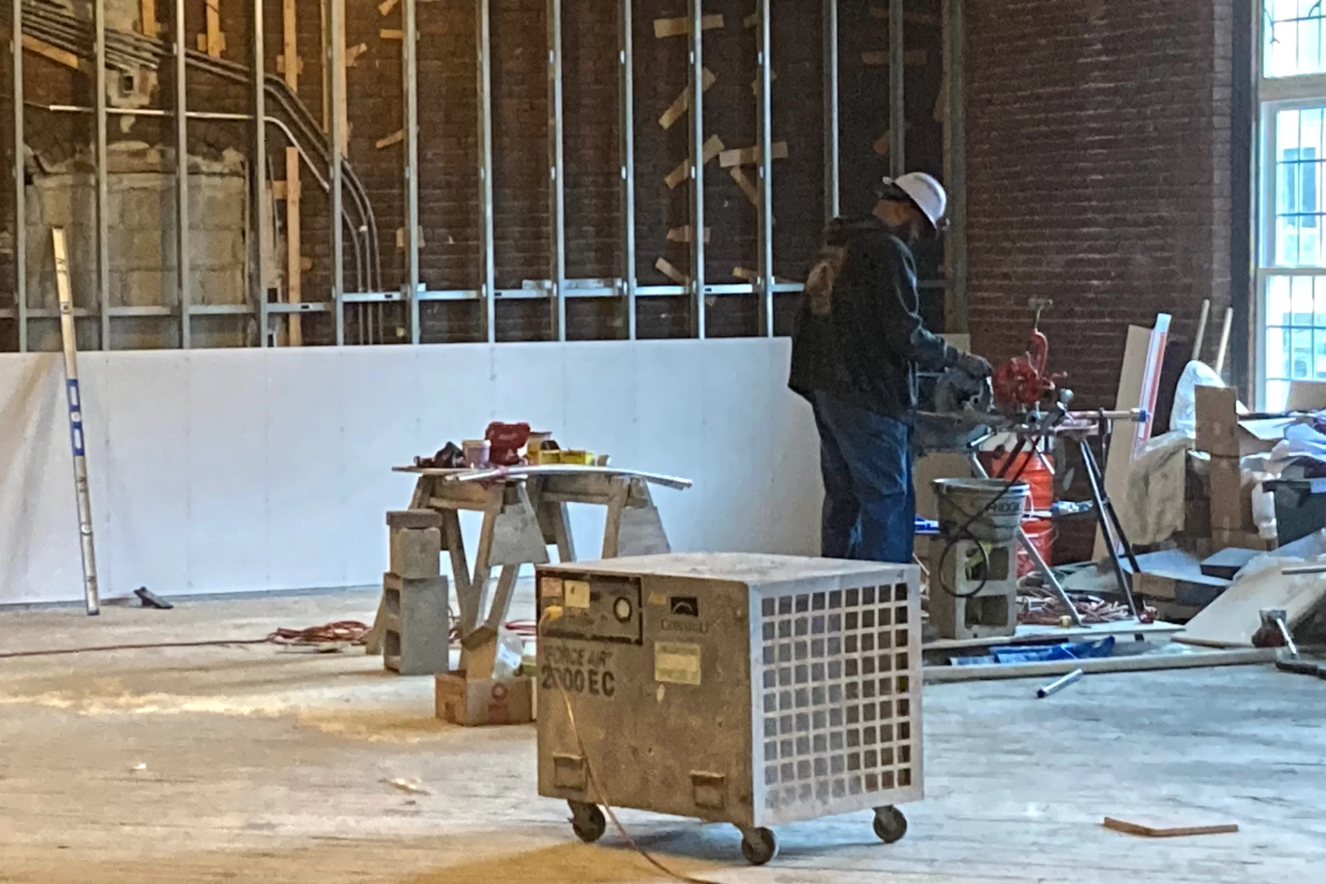 Its spaciousness has made Chase Hall Lounge broadly useful during the renovation, even as it has undergone its own alterations. Here a pipefitter cuts threads in a section of pipe. The new wallboard in the background will conceal a wall that once incorporated a doorway — indicated by the gray concrete blocks. (Doug Hubley/Bates College)