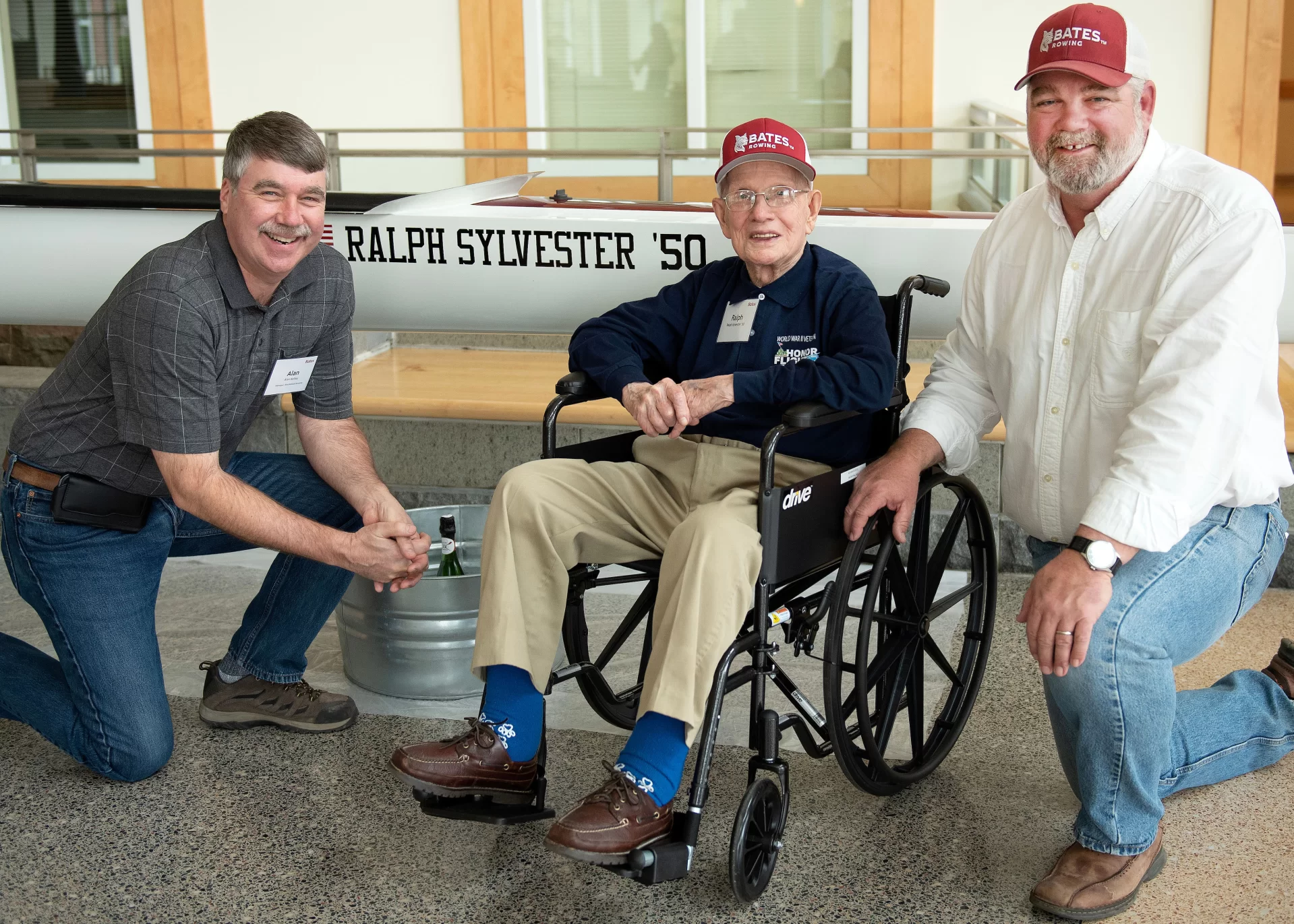 Mechanical Services Manager Alan Kelly, left, Ralph Sylvester ’50 and Bates Rowing Head Coach Peter Steenstra pose for a portrait in front of the new Bates rowing shell at Perry Atrium in Pettengill Hall on April 29, 2023. Coach Steenstra presented Sylvester with a blade during the dedication ceremony making Sylvester the only non-rower to receive one.