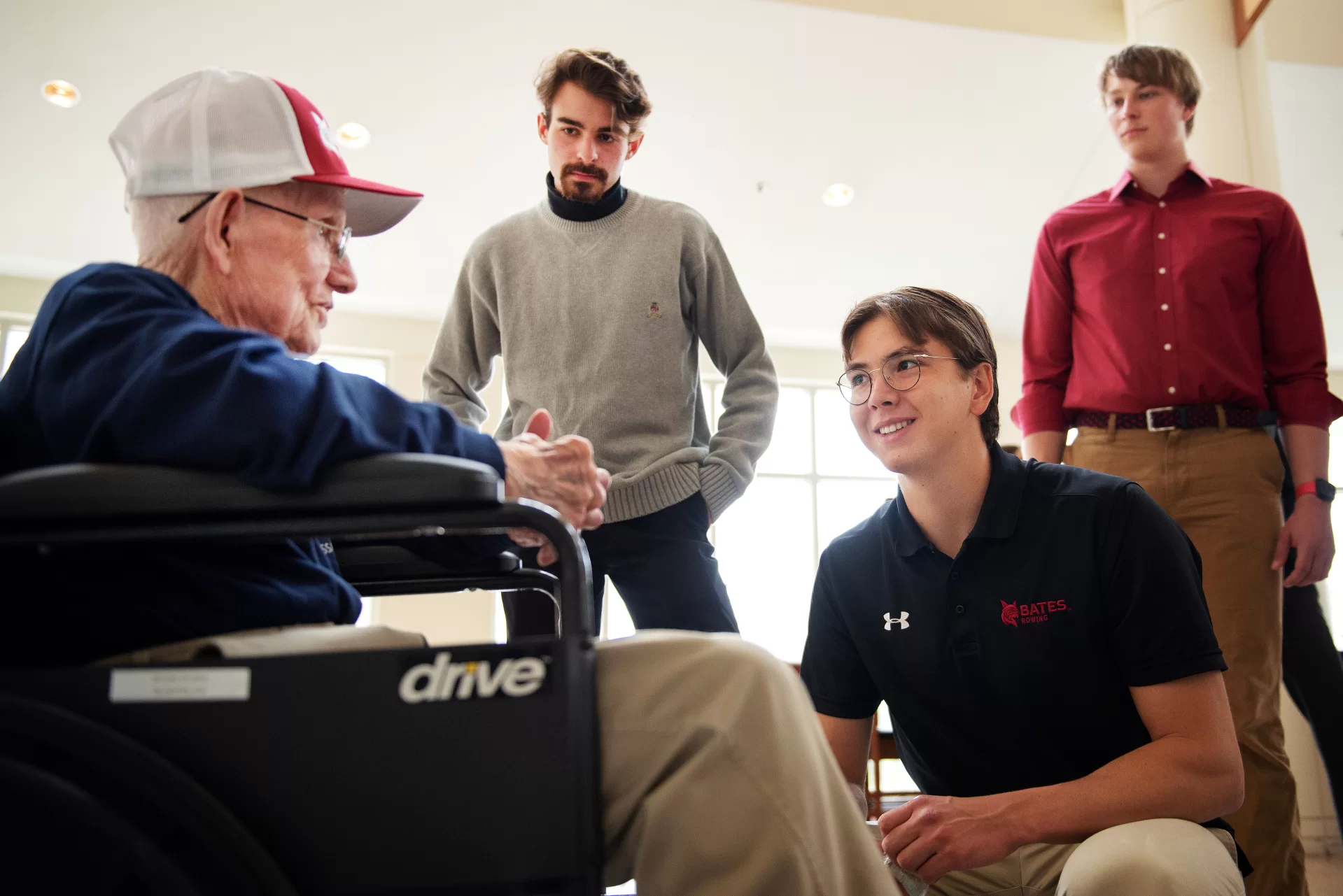 Ralph Sylvester ’50, left, talks with members of the Bates rowing team Aidan Braithwaite ’23 of Milton, Mass.; Isaac Levinger ’24 of Rockville, Md.; and Charles Renvyle ’25 of Hopkinton, N.H. during the dedication of the new rowing shell at Perry Atrium in Pettengill Hall on April 29, 2023.