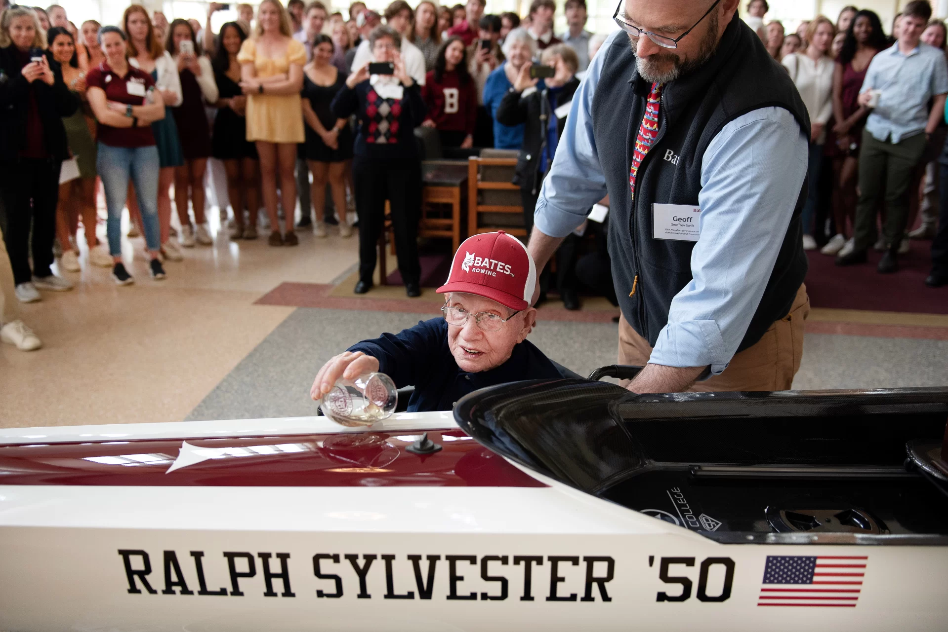 Ralph Sylvester ’50 christens the new rowing shell at Perry Atrium in Pettengill Hall on April 29, 2023. Bates Rowing Head Coach Peter Steenstra presented Sylvester with a blade during the dedication ceremony making Sylvester the only non-rower to receive one.