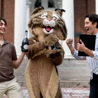 The Bates Bobcat (played by BCO writer Freddie Wright) tours Lake Andrews and the historic Quad with BCO designer Kirsten Burns. On left, in brown shirt, William Spencer Orto Symmans ’23, whose neuroscience thesis is titled “ A Data-Drive Taxonomy of Olfactory System Principal Neurons.” On right, in striped shirt, Evan Koch ’23, whose neuroscience thesis (adviser: Jason Castro) is titled “A Comparative Analysis of Gene Expression in the Dorsolateral Prefrontal Cortex of Autistic Individuals Across Age and Sex.”