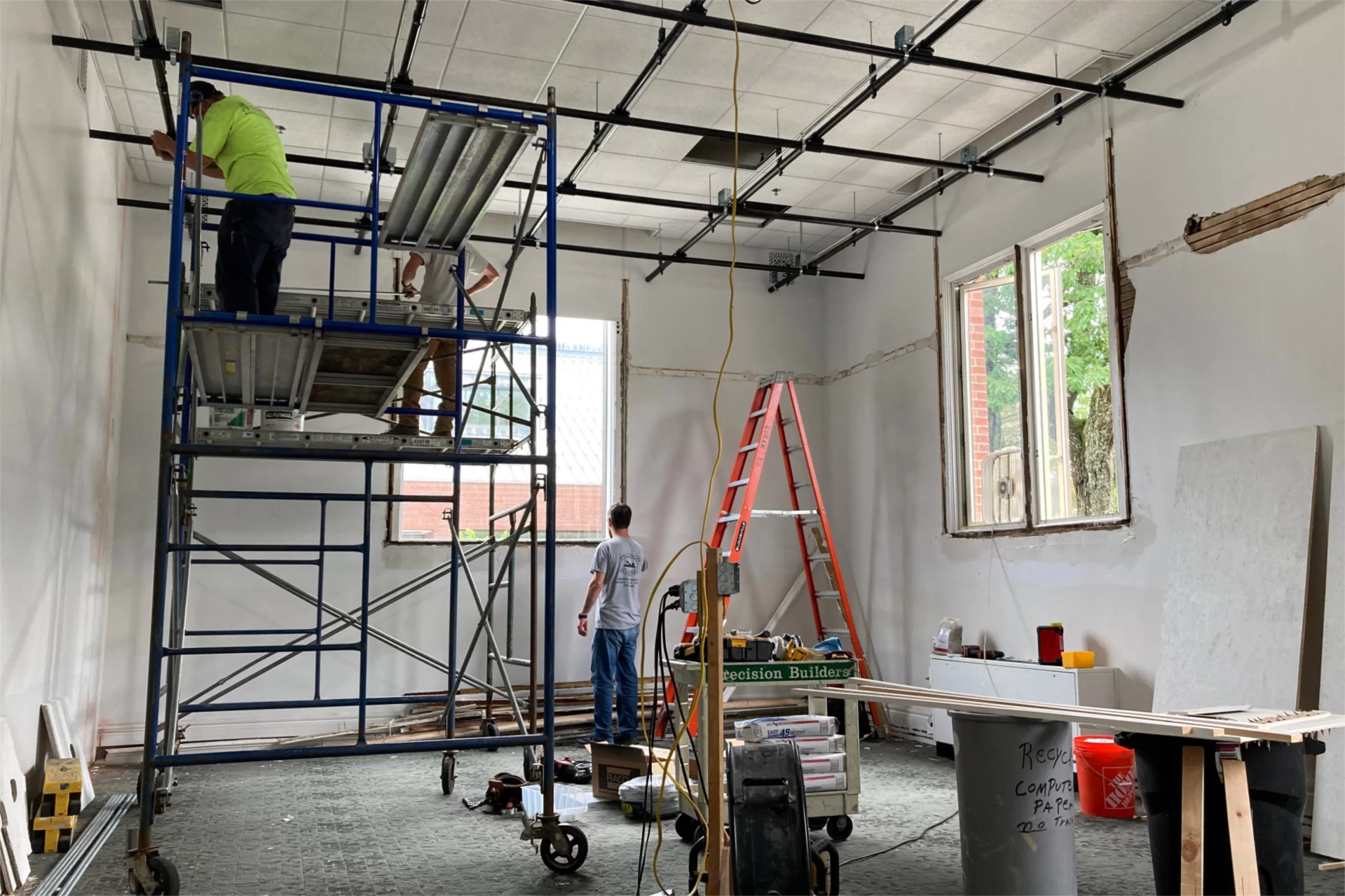 On the staging, electricians make connections on the ceiling grid that will support imaging and sound equipment when the conversion of Coram 110 into an immersive media studio is complete. At floor level is a carpenter. (Doug Hubley/Bates College)