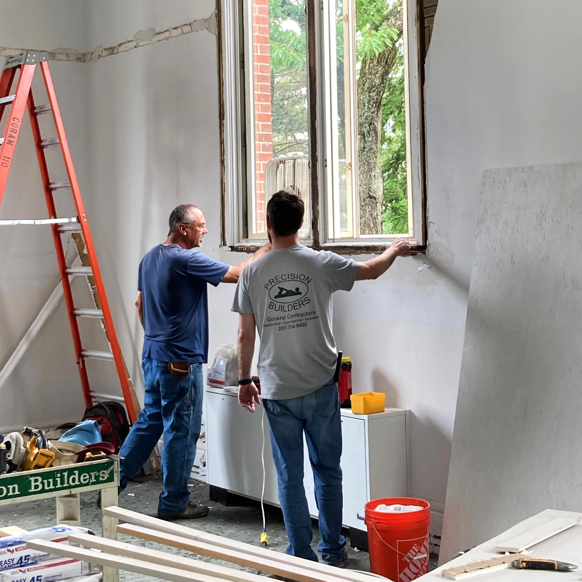 Precision Builders staff examine a window frame bound for removal in Coram 110. (Doug Hubley/Bates College)