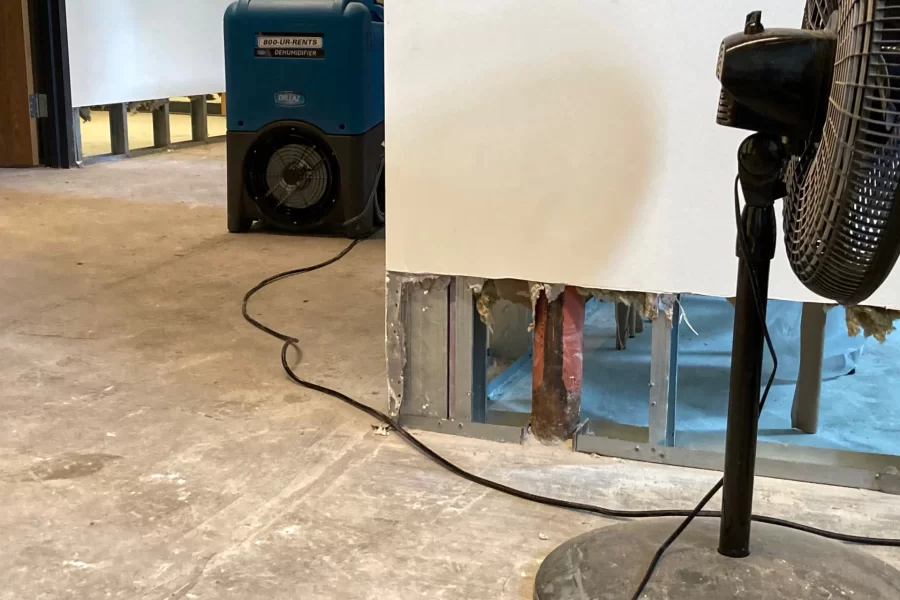 An Aug. 1 image from the Student Affairs office suite shows the aftermath of the July 25 rain: new carpet has been discarded, a 12-inch strip of wallboard removed, and a dehumidifier and fan are drying things out. (Doug Hubley/Bates College)