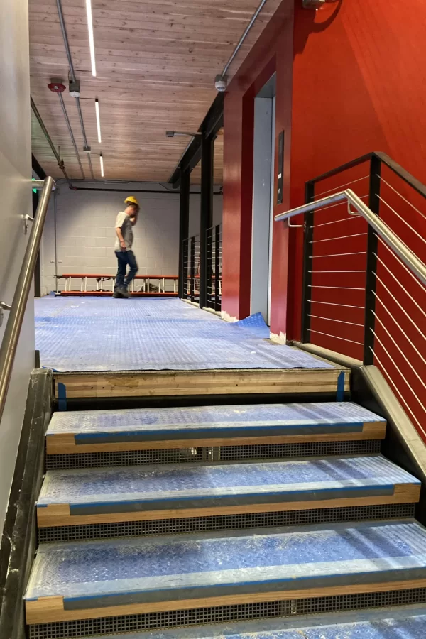 A view of the Central Stair and its elevator. Note the stylish new handrails. The blue plastic floor protection conceals oak stair treads and flooring (visible overhead) made from cross-laminated timber. (Doug Hubley/Bates College)