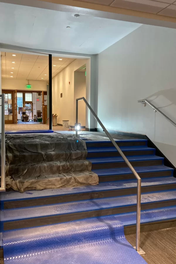 The stairs and corridor to Memorial Commons have been snazzed up with new paint, floor and step coverings, and handrails. The blue material provides temporary protection to the new flooring. (Doug Hubley/Bates College)