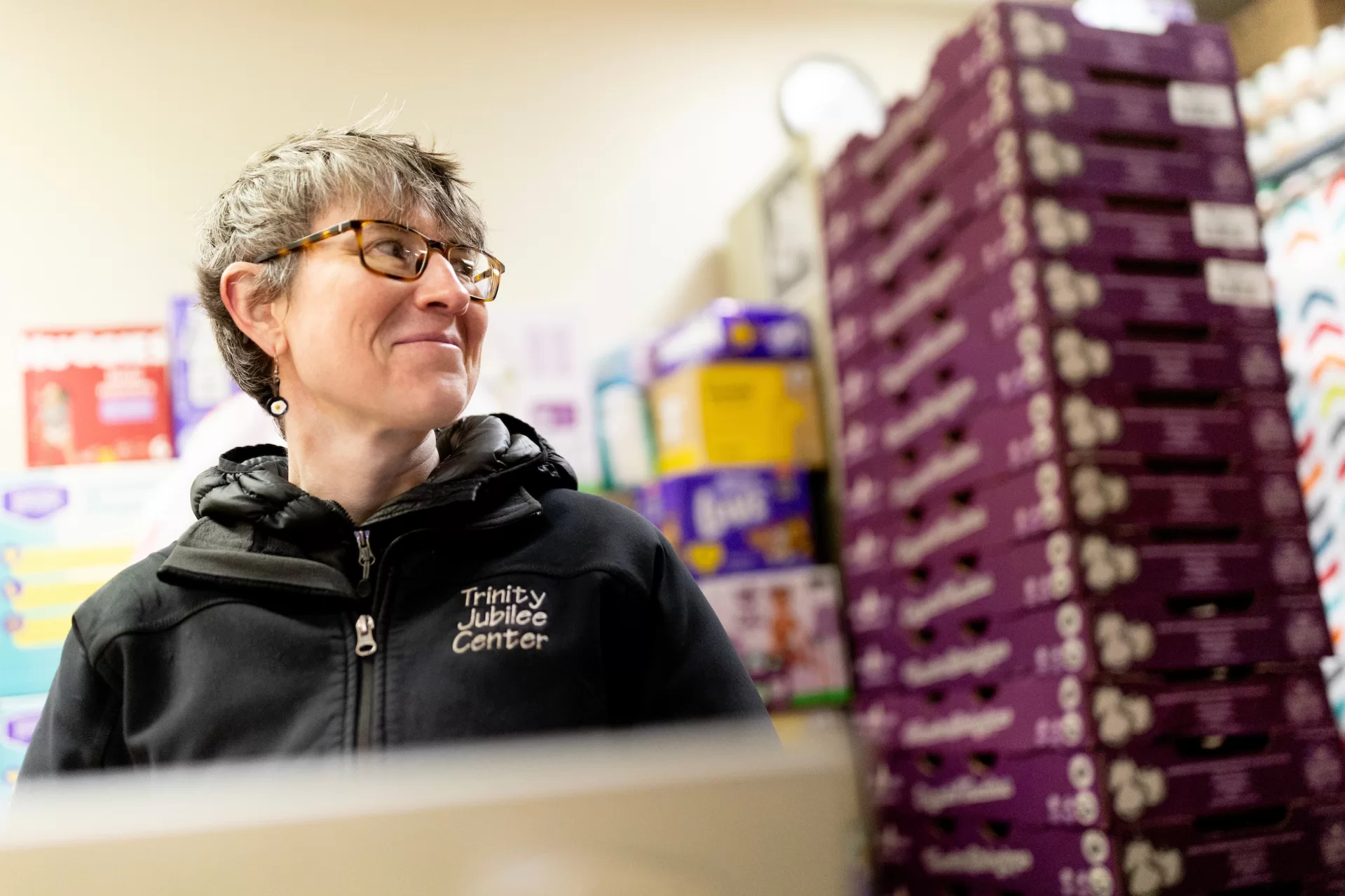 Erin Reed ’08, executive director of the Trinity Jubilee Center in Lewiston, works in the organization’s food bank on Nov. 30, 2023, after which she relocates into the center’s shelter while on her computer. Shown with her mentor and retired ED Kim Wetlauffer ’80.