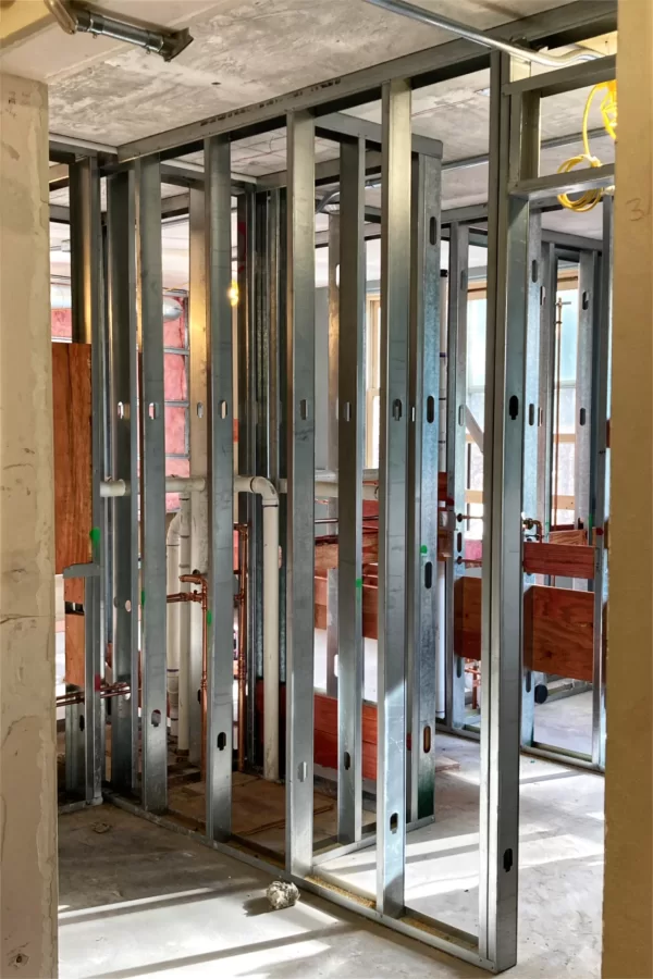 Wall studs are complete and in-wall utility connections are in progress in this third-floor restroom. The red-tinted plywood, called “blocking,”will provide solid attachment points for fixtures. (Doug Hubley/Bates College)