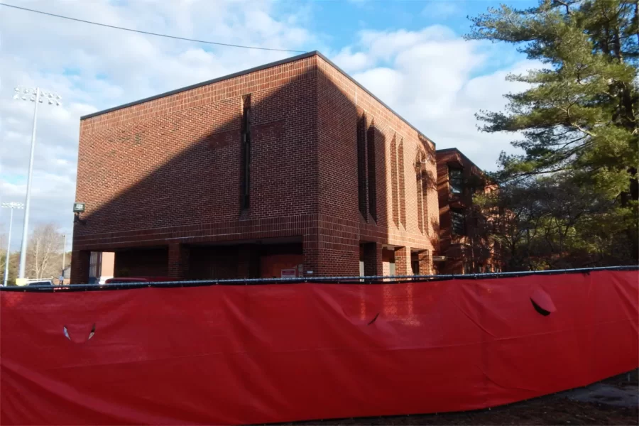A three-quarter view of 96 Campus Avenue from the street. Concealed behind the construction site fence is the former main entrance. CCU was interested to see that in a first for a construction project at Bates, management firm Consigli Construction eschewed the forest green that was its longtime choice for fence fabric in favor of a red similar to its corporate color. (Doug Hubley/Bates College)