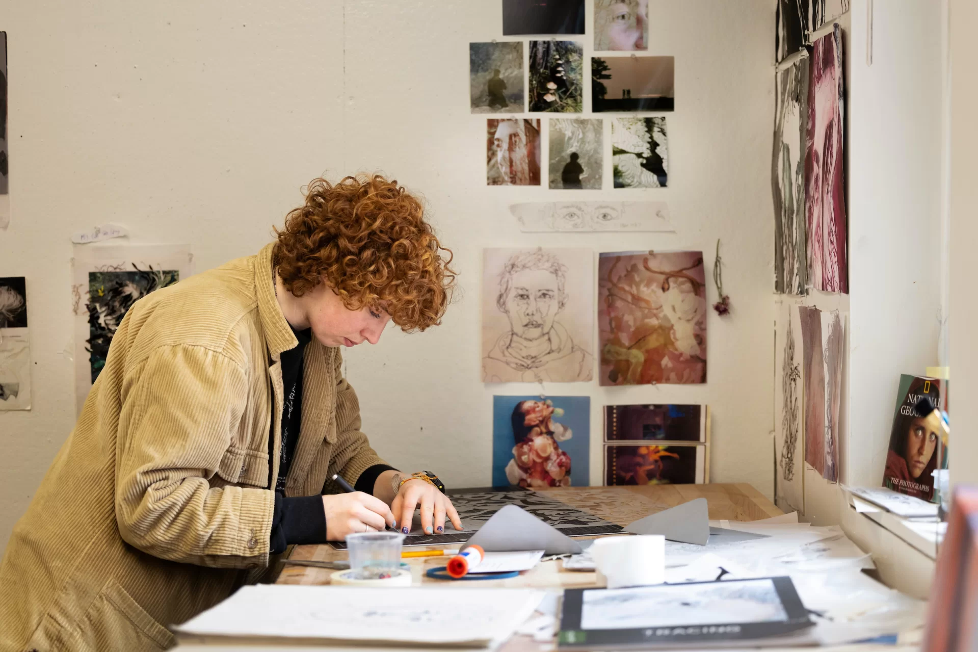 Studio art major Emma Upton ’24 of Amherst, N.H., in her Olin Arts Center studio on March 5, 2024.

Artist Statement
“Fragmentation, 2024

This series is founded within the context of the October 25th mass shooting in Lewiston that left our community reeling in sorrow, fear, and mourning. In the days that followed, I found myself in a state of numb disbelief within the surreal limbo of lockdown. In an attempt to process my emotions, I turned to art. I created a series of 50 continuous line self-portraits that seek to illustrate my internal state of sorrow and uncertainty. These portraits became the foundation of my work which involved abstracting the original self-portraits using a variety of techniques and mediums.

I found abstract forms within the interconnected lines and pulled the found-forms out to create a series of new abstract portraits. I then traced, layered and collaged these portraits with pages from magazines. I cut away some of the forms to reveal either the layers of colorful paper beneath or light shining through the cut forms. Finally, I covered the abstractions with epoxy to provide a translucent finishing effect through which light can shine.

As a culmination to my work, I created a final piece composed of fragmented mirrors and stained glass. The material is fundamentally connected to the initial experience during the lockdown, because it incorporates the same fractured mirrors that I looked into while creating the 50 original self-portraits. I cut, reconfigured and redefined the mirrors into an abstracted self-portrait drawn from the forms found within the original sketches. The use of stained glass creates a transparent effect and enables the use of lighting that is a uniting element within this series. The reflective quality of the mirror actively engages and incorporates the viewer.

The series is an expression of my personal experience during the lockdown that explores themes of loss, mourning, introspection, and unity. This work is in