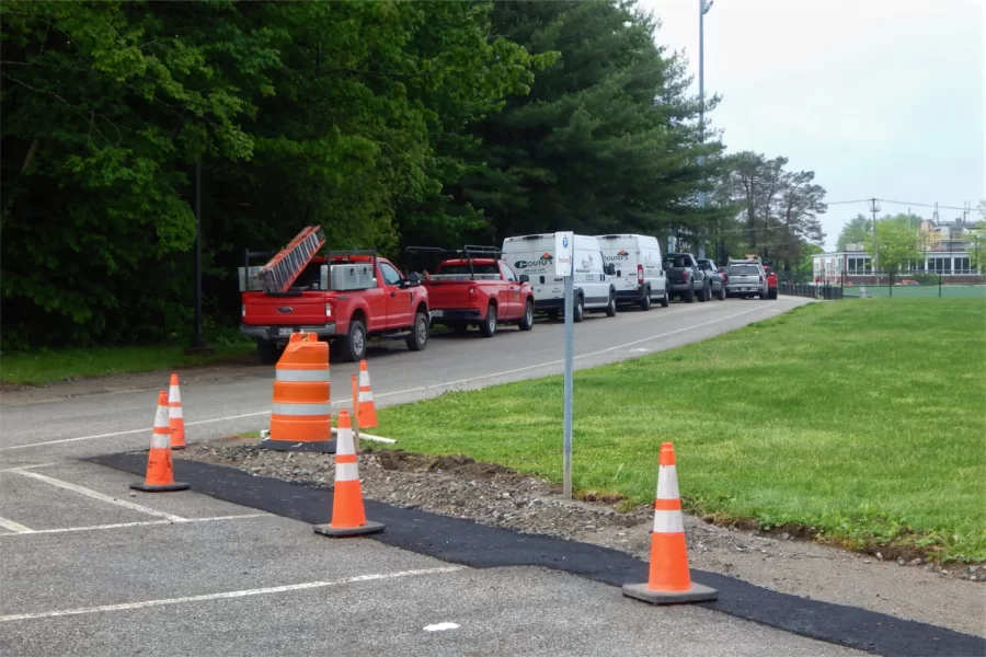Shown is part of a future route for a walkway connecting the new 96 Campus Avenue dorm (out of view up the road) to the center of campus. Where the vehicles are now parked, a sidewalk will run from the dorm to a point facing the orange cones. The cones show where a painted lane will lead to an existing path past Merrill Gym that, near the Bobcat statue, intersects with a main east-west footpath. (Doug Hubley/Bates College)