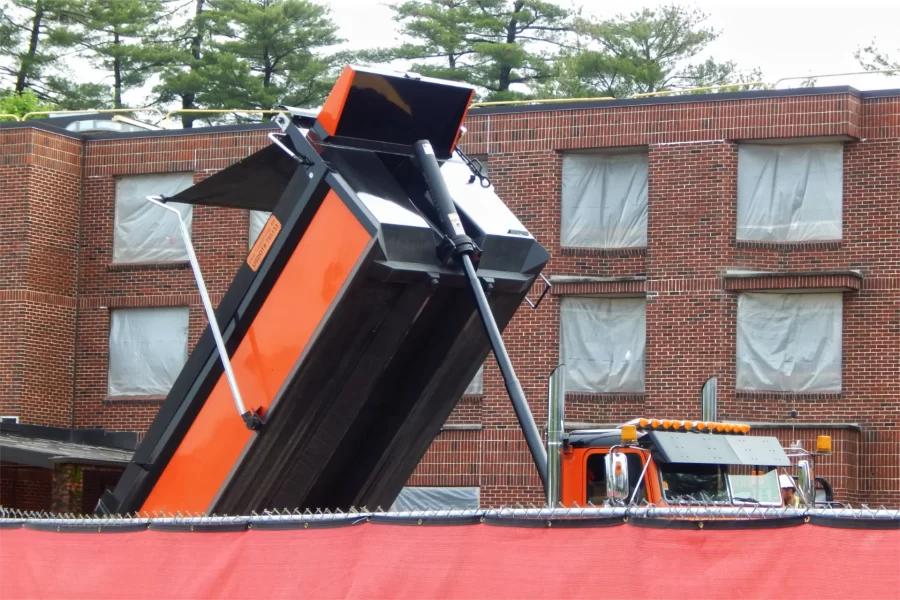 Inside the 96 Campus Avenue construction site fence, a truck dumps asphalt as a paving crew tops the parking lot. (Doug Hubley/Bates College)