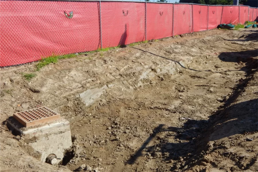 This excavation at the 96 Campus Avenue parking lot entrance will be landscaped into a swale for handling storm runoff — as evidenced by the drain at left. (Doug Hubley/Bates College)