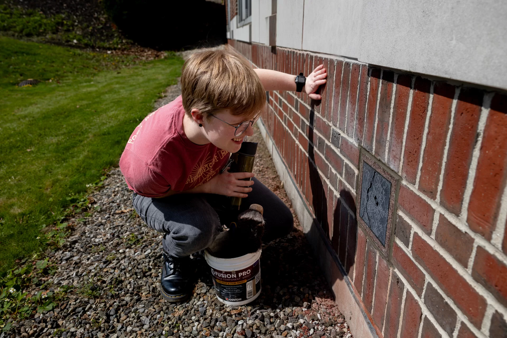 E.J. Holm admires the 2025 ivy stone featuring their design, an abstract line map of downtown Lewiston–Auburn, after helping Ron Tardif install the stone. (Phyllis Grabe