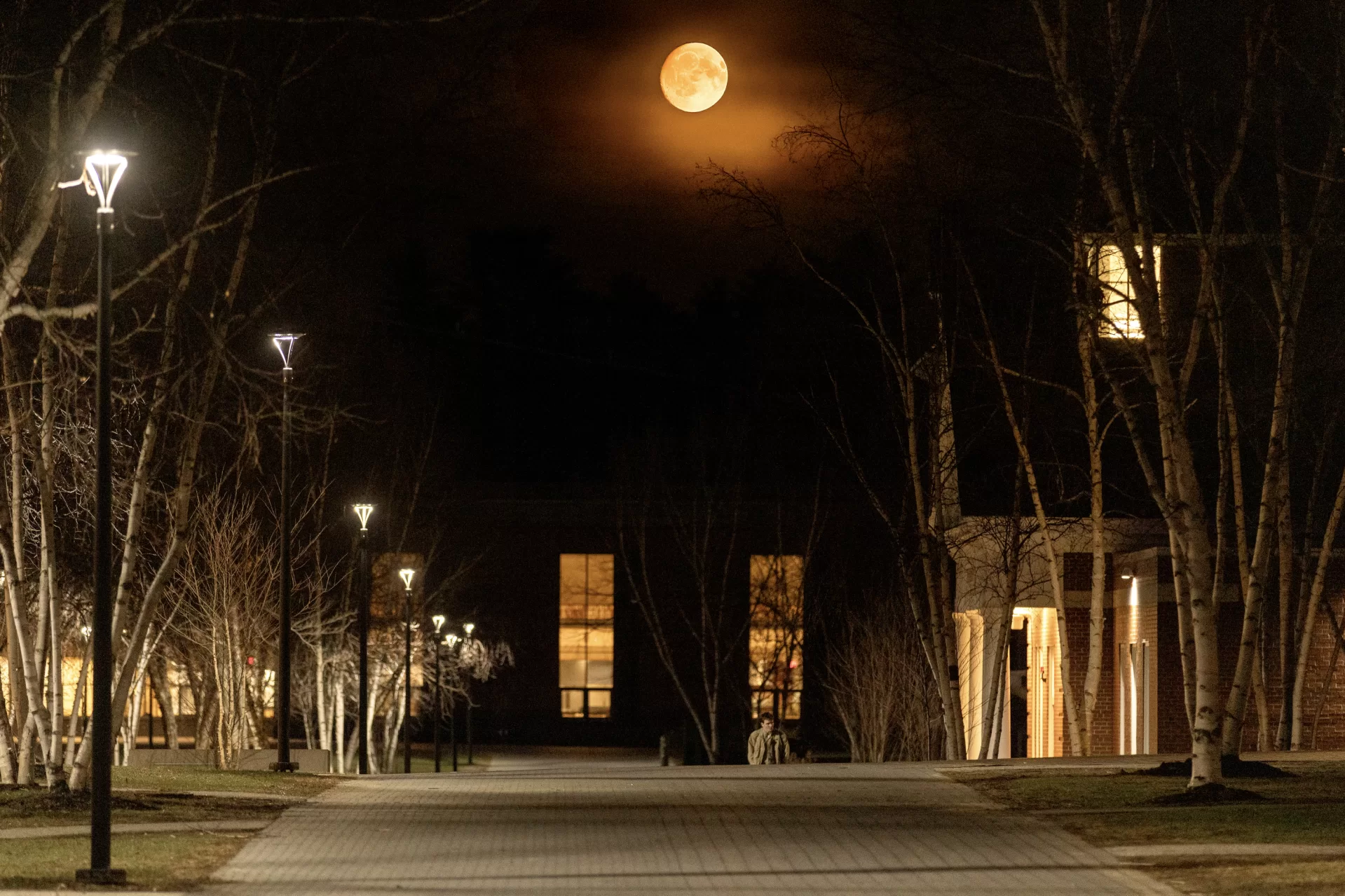 Orange moon captured on 15 April 2025 layered from other images and long exposures to create best image. “We got a text: ‘Look up at the moon.’” — Amelia Wright ’28 (left) of Haddonfield, N.J., and Lila Hutchins ’28 of Silver Spring, Md., had just finished a night of studying when the message lit up their group chat. Stepping outside Parker Hall, they looked up and found the sky glowing. The photograph, taken at about 9:30 p.m. on April 14, 2025, by Sammy Weidenthal ’27 of Chagrin Falls, Ohio, is a composite of long exposures showing the orange moon as it rose over Alumni Walk, just before the clouds rolled in. What the students saw was caused by scattering of light in Earth's atmosphere. When the moon is low in the sky, the light passes through more of the atmosphere, and the atmosphere tends to scatter more short wavelength (blue) light, leaving relatively more long wavelength (orange or red) light. (Sammy Weidenthal ‘27 for Bates College)