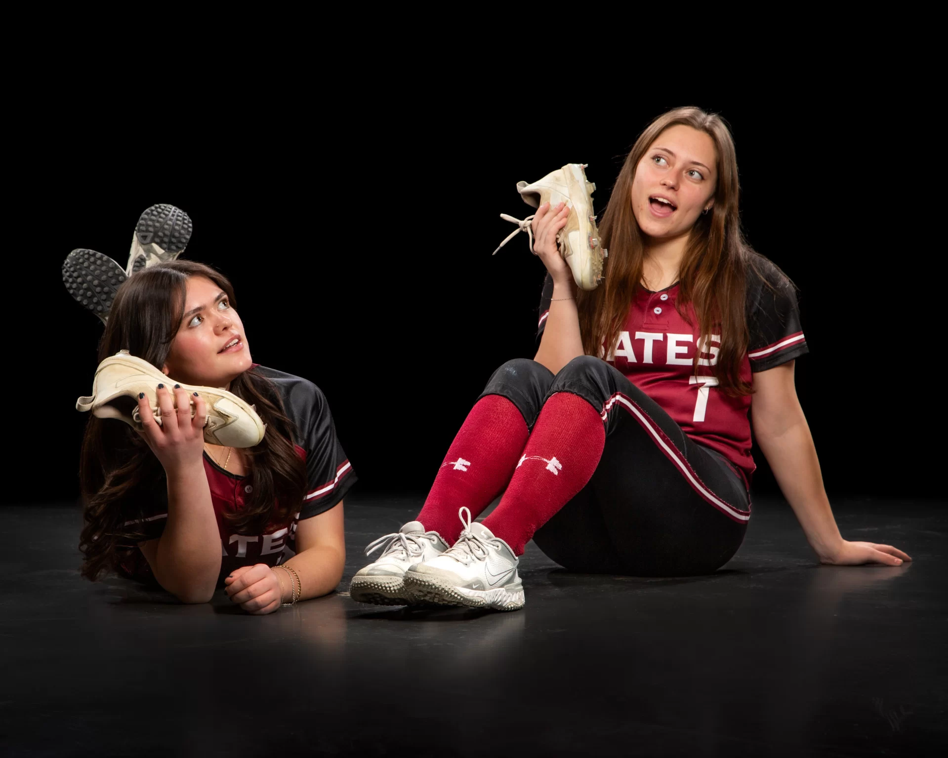 two softball players pretending to talk on the phone on shoes