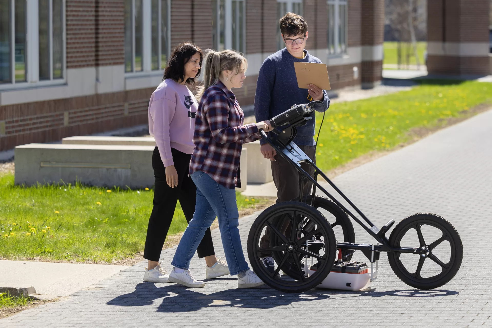 Early in May, students in Assistant Professor of Earth and Climate Sciences Shreya Arora’s Short Term course searched for an underground passage between Lane and Pettengill halls. Under their professor’s guidance, Caroline Friedman ’25 of Mercer Island, Wash., and Will Morris ’27 of Wayland, Mass., used a Ground Penetrating Radar (GPR) machine — purchased with funds from a startup grant— to investigate subterranean Alumni Walk. Later in the day, their classmates took turns with the GPR, after posing for a group photograph with Arora. Arora’s course “Earth Science Methods: Data to Discovery” allows students to master technical equipment, a valuable skill that enhances critical thinking, problem-solving, and employability. The hands-on and outdoor-focused unit provides training on a wide range of tools, including GPS, Real-Time Kinematics (RTK), and drones. These instruments have broad applications, says Arora. For instance, GPR, a geophysical tool used to scan the subsurface, is commonly employed to locate corroded or leaking pipelines, uncover hidden archaeological artifacts, unmarked graves, weapons, or identify geological features such as faults, which are critical to map before constructing dams or tunnels. This course will equip students with technological literacy and prepare them for academic or industry-based research.