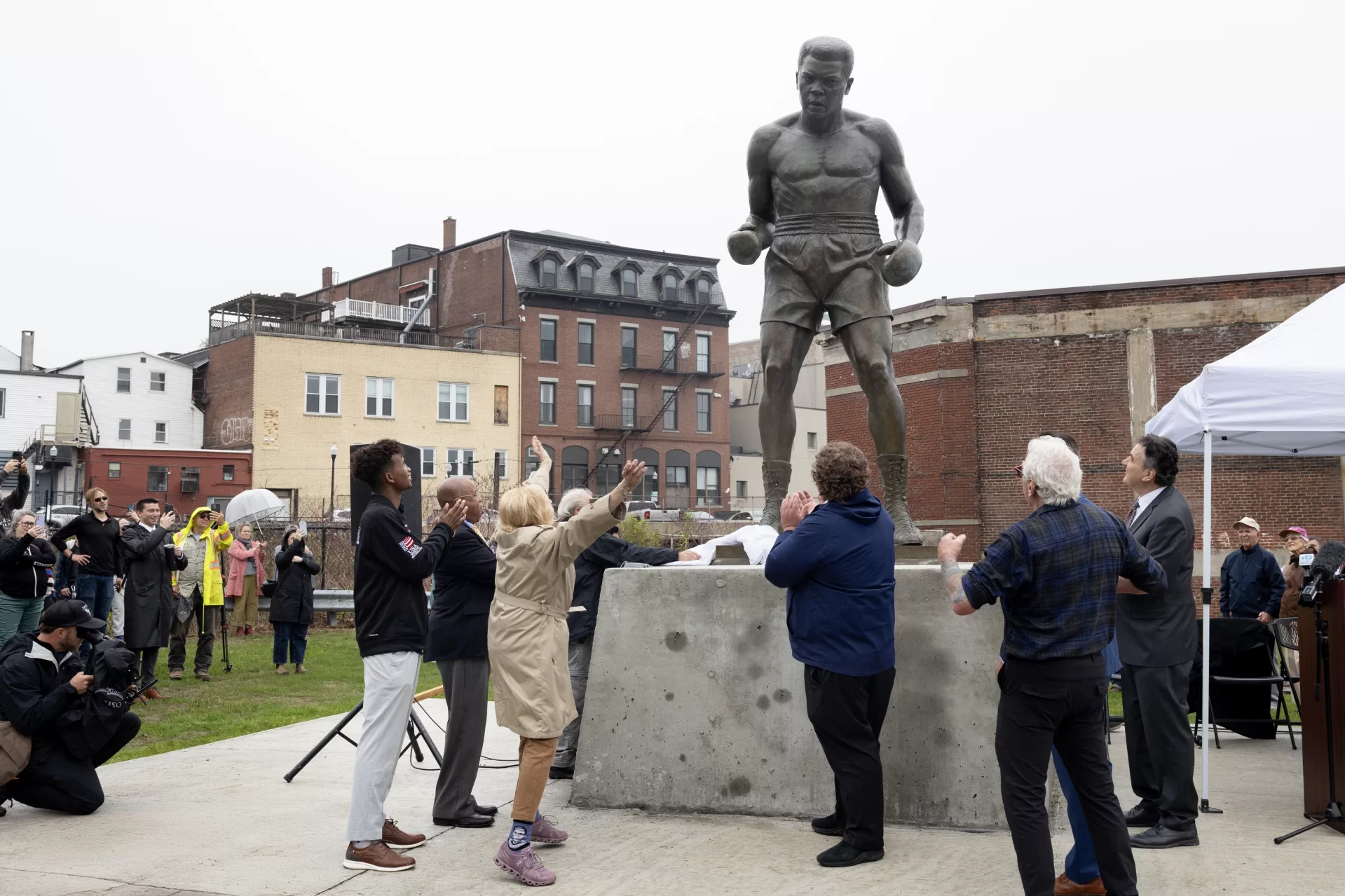 https://www.sunjournal.com/2025/05/31/citys-new-guardian-statue-of-muhammad-ali-challenges-encourages-reflects-lewiston/
On Saturday. May 31, at 2 p.m. a large crowd gathered undeterred by rainy weather to watch the unveiling of the Muhammad Ali statue after it had been installed Friday.
The statue overlooks Bates Mill No. 5 at 65 Main St., just 200 feet from the Auburn bridge. It is positioned near the city’s “Hopeful” sign by artist Charlie Hewitt, who co-initiated the statue project with Platz. It represents the “loud, proud, strong, resilient” spirit of Lewiston, in the words of Gov. Janet Mills, who spoke at the unveiling.
Among those in photos:
Tom Platz, a developer and principal at Platz Associates
Philadelphia-based sculptor Zenos Frudakis
Lewiston Mayor Carl Sheline
Maine Governor Janet Mills
Bates President Garry W. Jenkins
City Administrator Bryan Kaenrath
Ilyas Bashir ’25, a 22 Northern New England Golden Gloves champion and amateur boxer for Bobby Russo at the Portland Boxing Club.
Bashir’s mother Fatuma Hussein
Bashir’s younger brother Idris Bashir ’28, also a champion amateur boxer
James Reese with Bates students and one graduate, Mariana Kaluba ‘25
Benjamin E. Mays '20 Distinguished Prof of Rhetoric, Film, and Screen Studies Charles Nero
Rachel Ferrante ’10, Executive Director of Maine MILL
Ernie Ashton, shuttle driver
Patricia Lawson, from director of Bates College Relations