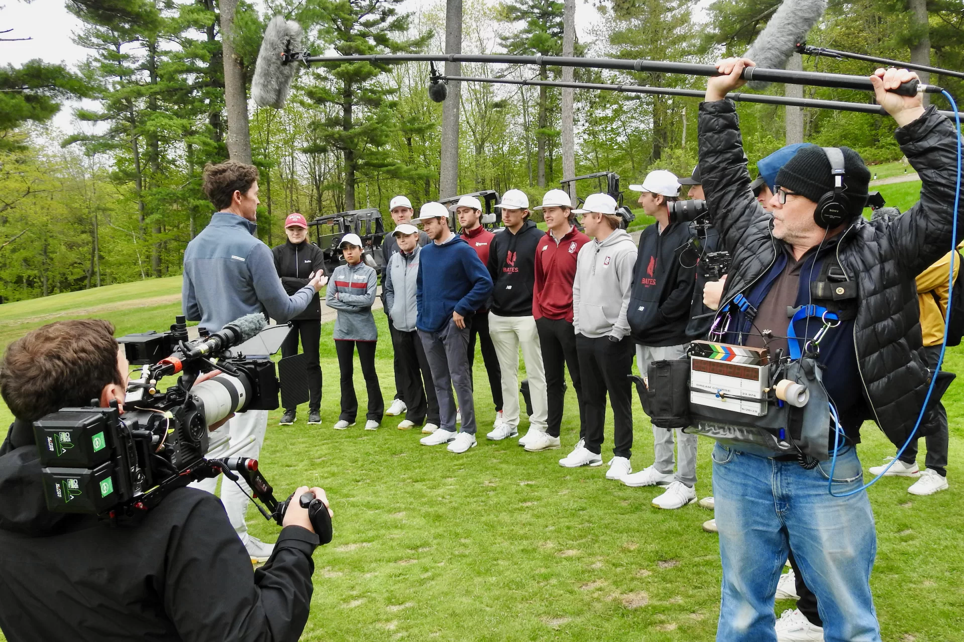 As members of the film production team capture video and audio, Derek Duncan (left), Golf Digest’s architecture editor, talks to the Bates golfers on the elevated 9th tee at Martindale Country Club in Auburn, Maine, on May 20, 2025. The Bates golfers were the stars of a branded video about Adobe Firefly, a new generative-AI tool. (Jay Burns/Bates College)