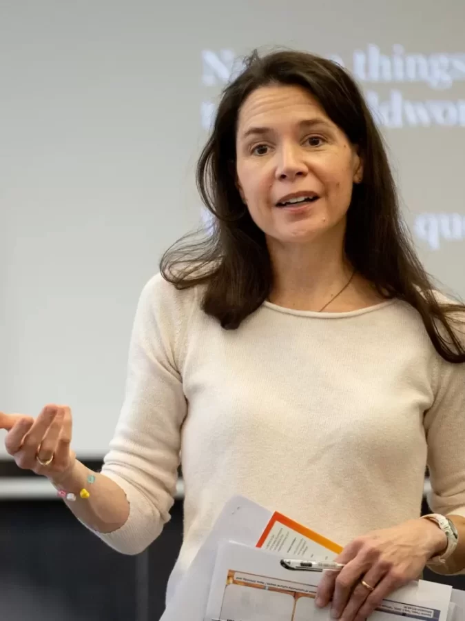 A woman standing and talking at the front of a classroom