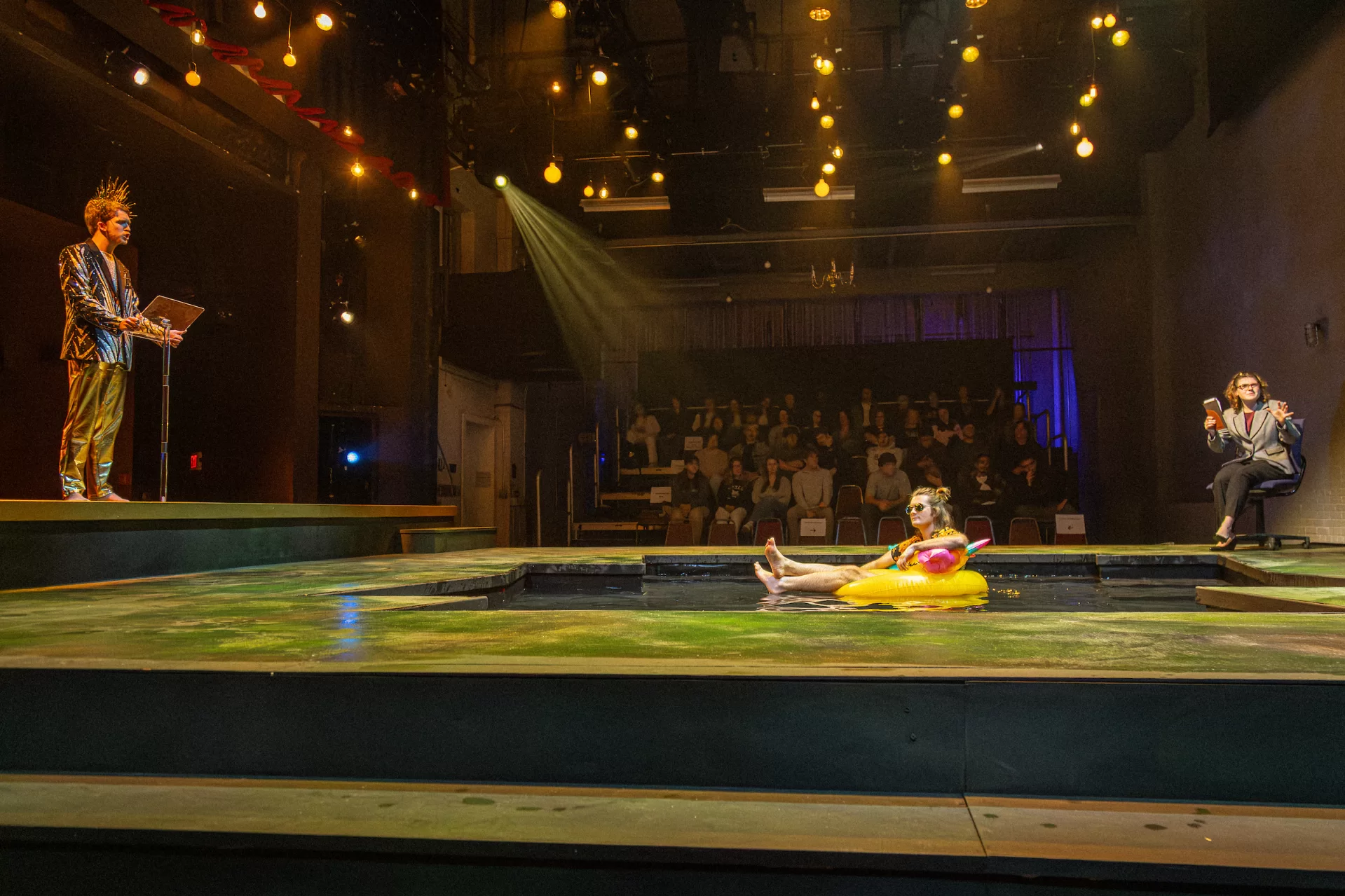 In one of the late acts in the Bates production of Mary Zimmerman’s Metamorphoses, the sun god, Apollo (Jack Hagan ’27 of Cape Elizabeth, Maine), sings to his son Phaeton (Graham Austin ’28 of Basalt, CO, center in the pool) as Phaeton laments over their difficult, limited relationship to the Therapist, played by Isabel Fronzaglia ’26 of York, Maine. (Sammy Weidenthal ’27 for Bates College)