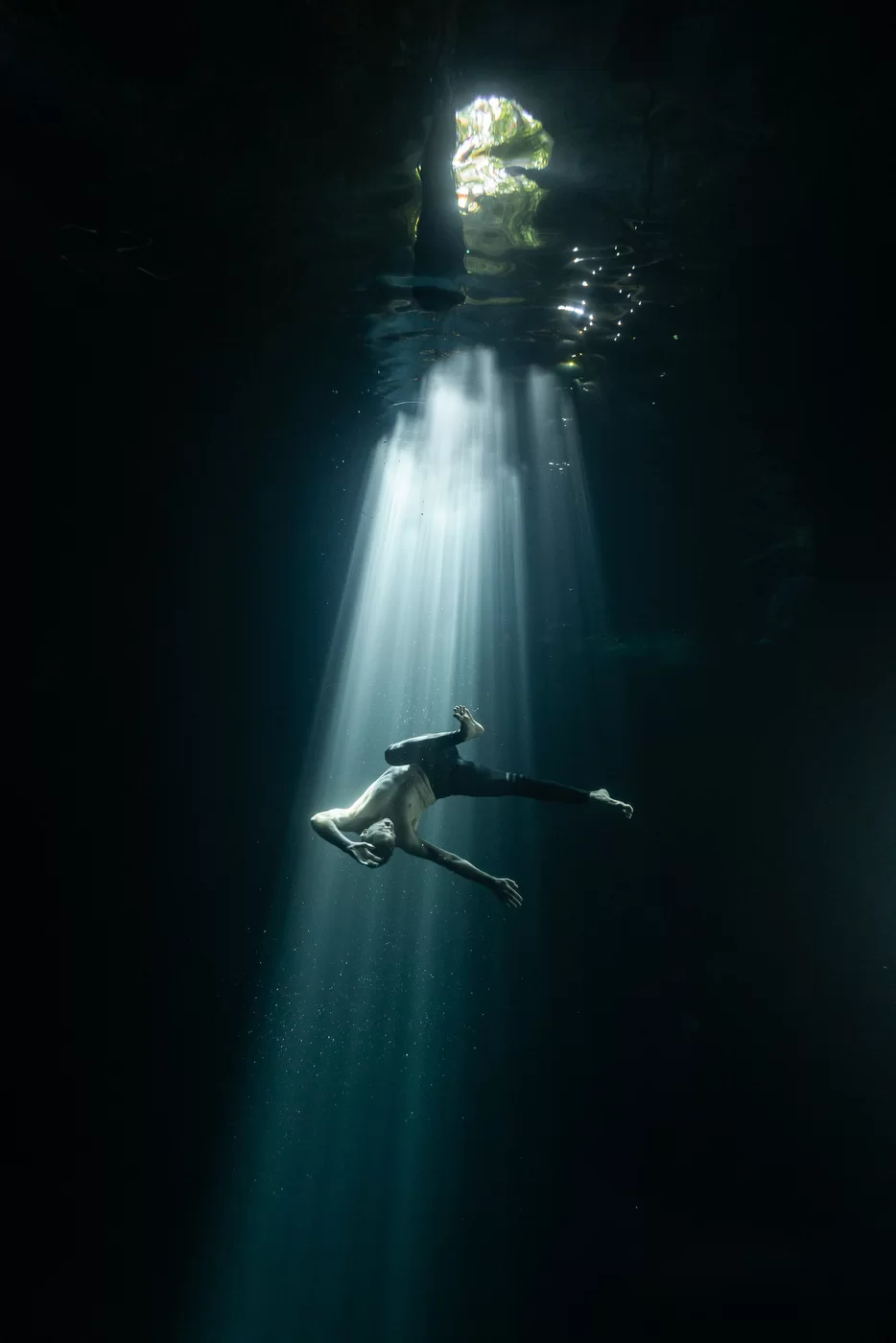 A man dances underwater, with light filtering in from above like a spotlight.