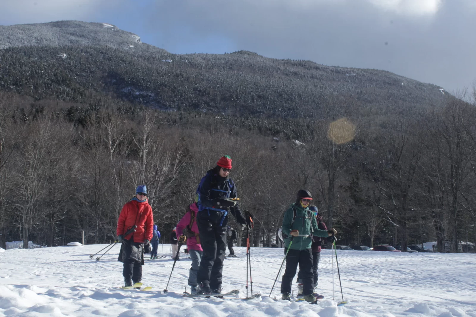 A group of people ski across snow with mountains in the background.