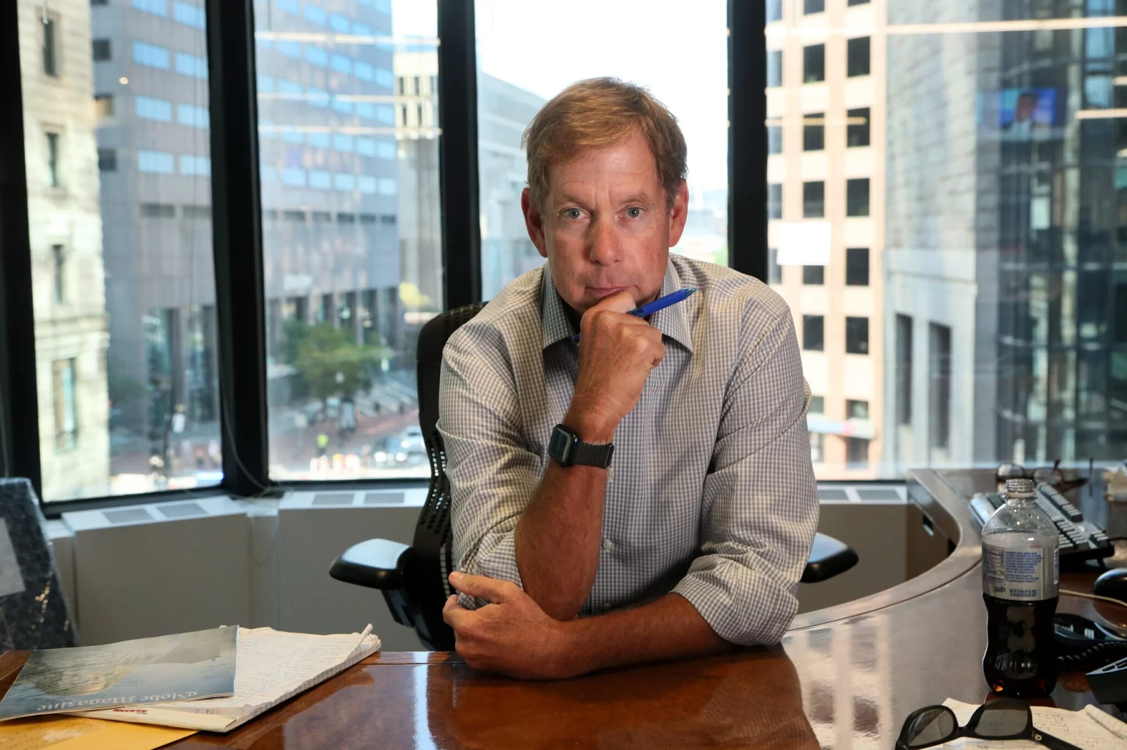 A man leans his forearm against a desk with a city skyline view in the background.