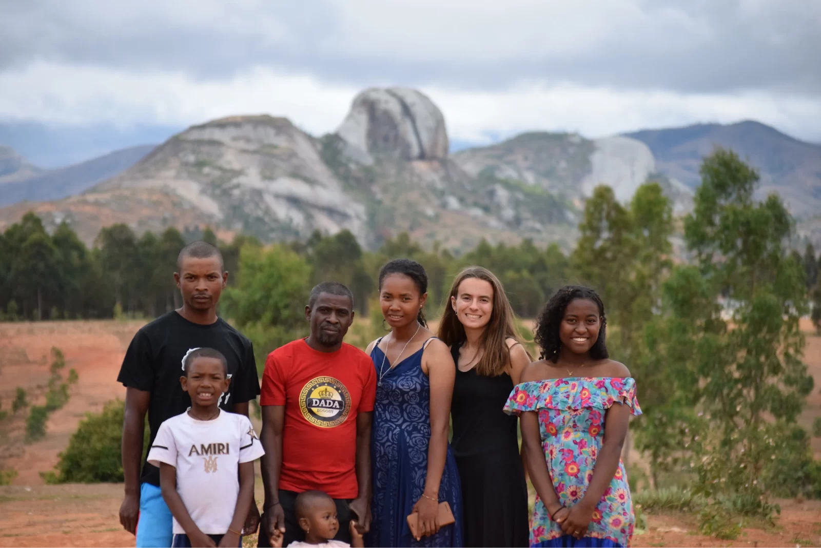 A group of people of different ages stand outside in front of a mountainous background.