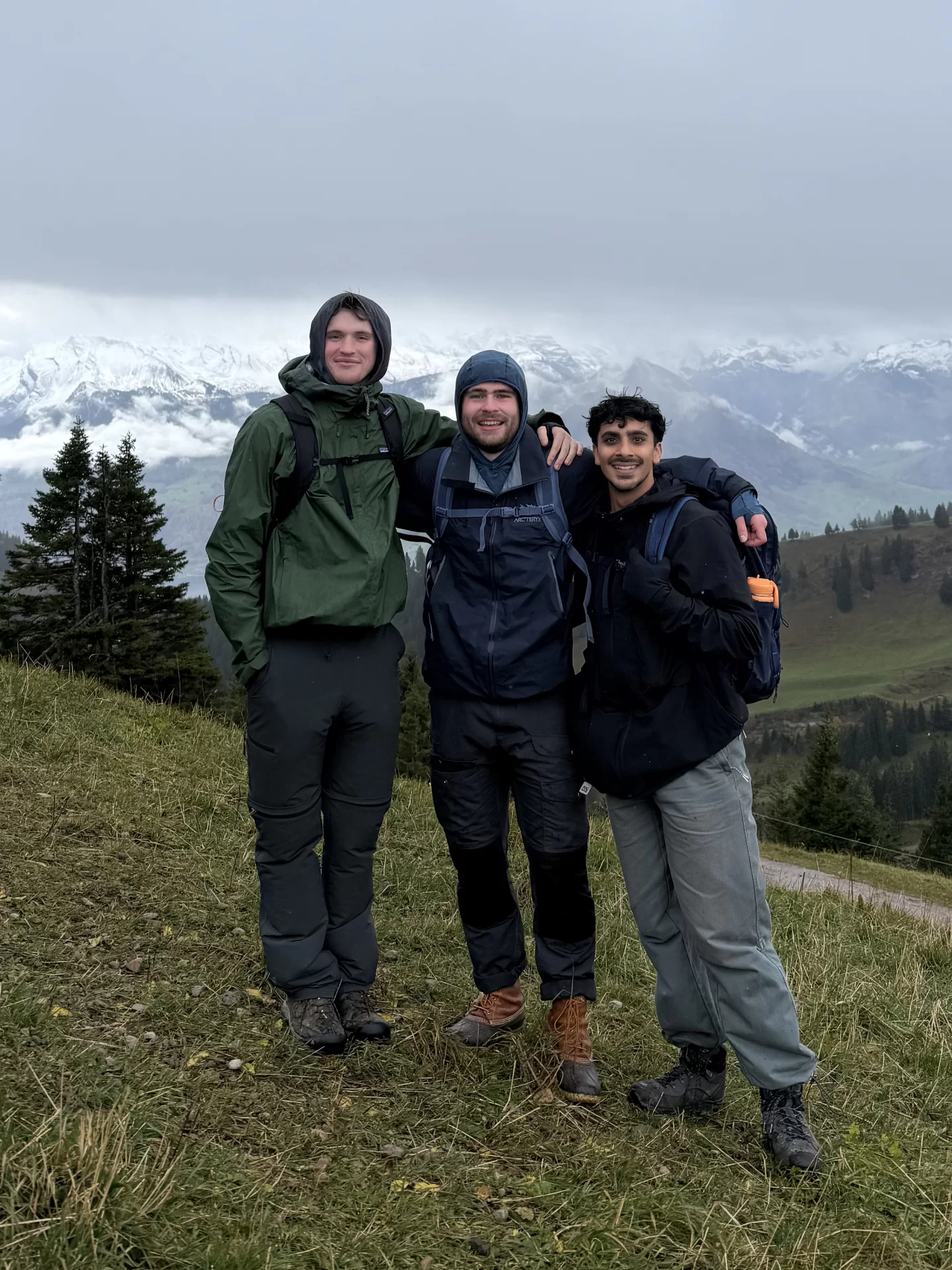 Three men pose during a hike with mountains in the background.