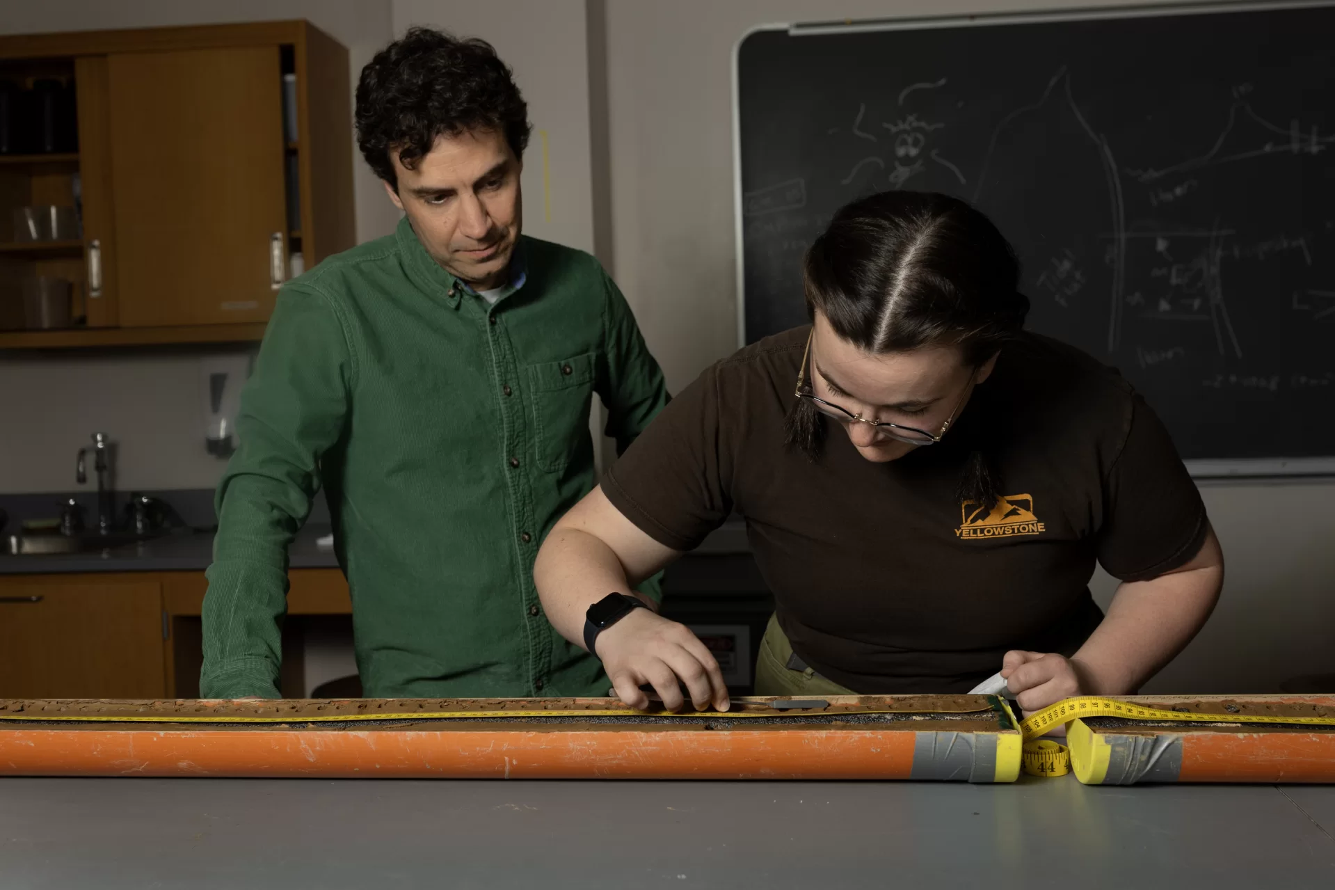 A man and a women examine a long sediment sample lying on a table in a scientific laboratory.
