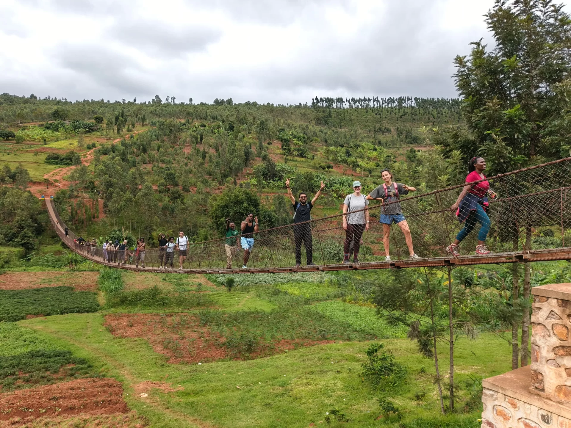 A group of people walk across a canopy bridge in front of a lush green landscape.
