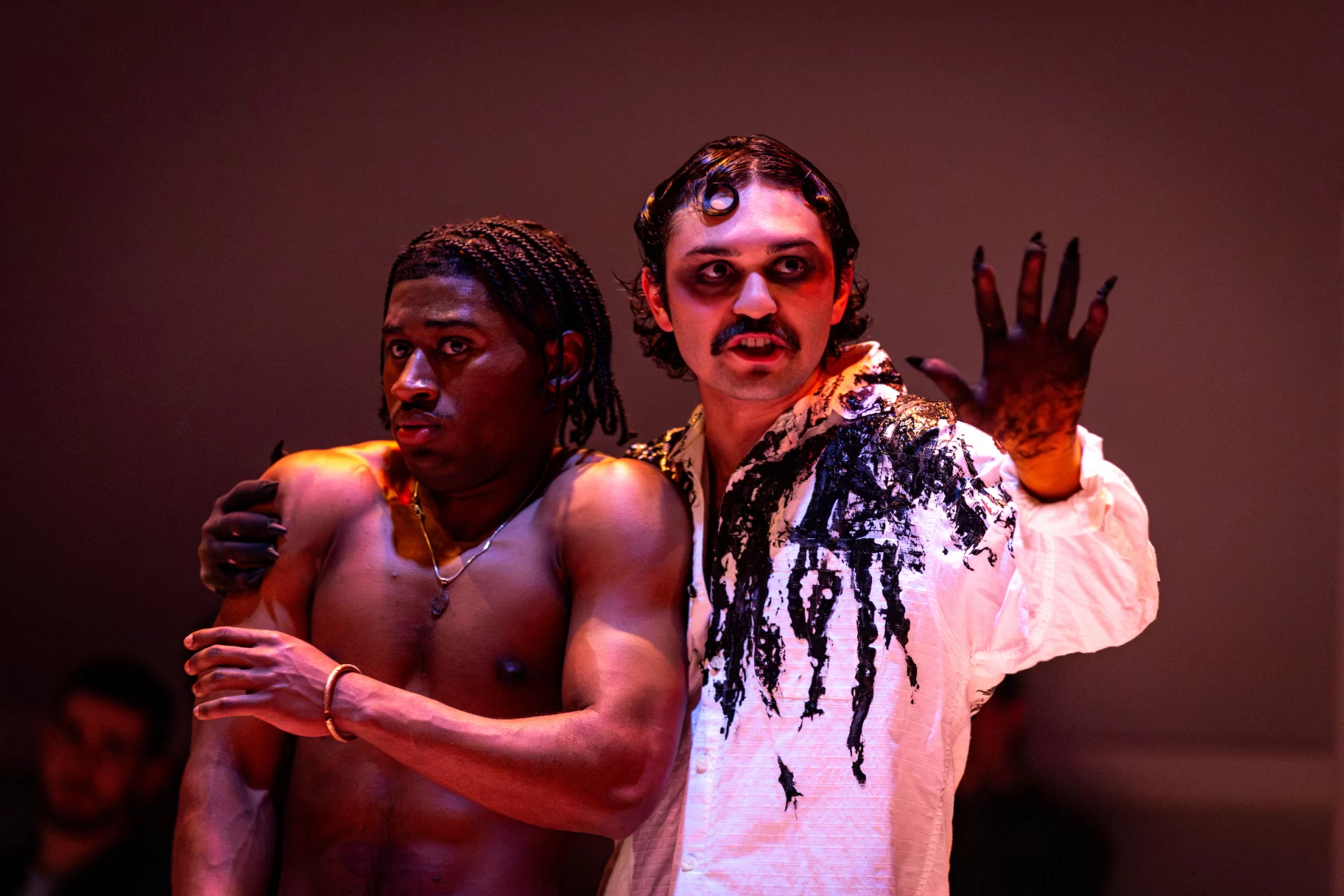 Two men pose on stage, one of them holding his hand up.