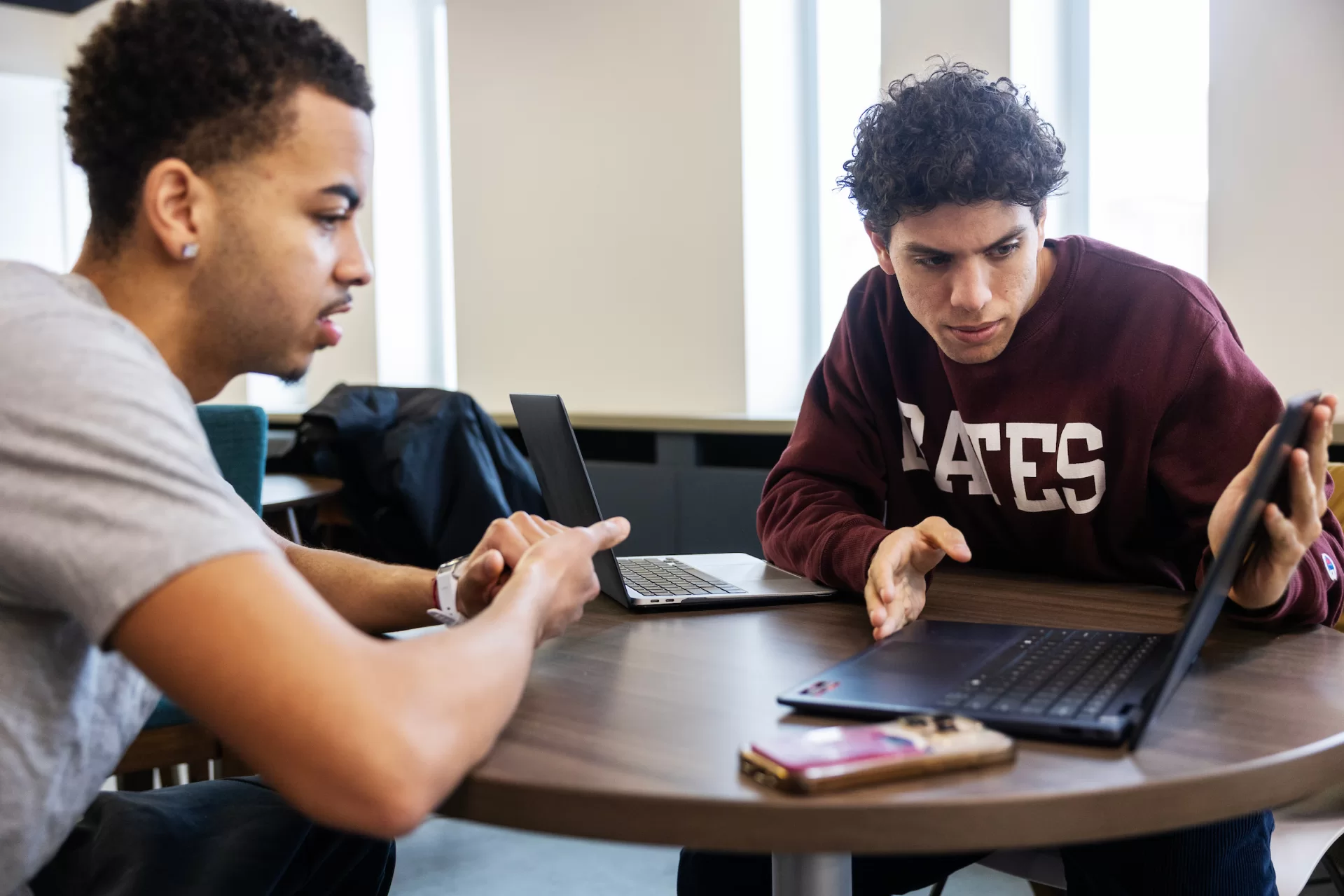 Two men look at a laptop screen while sitting at a table.