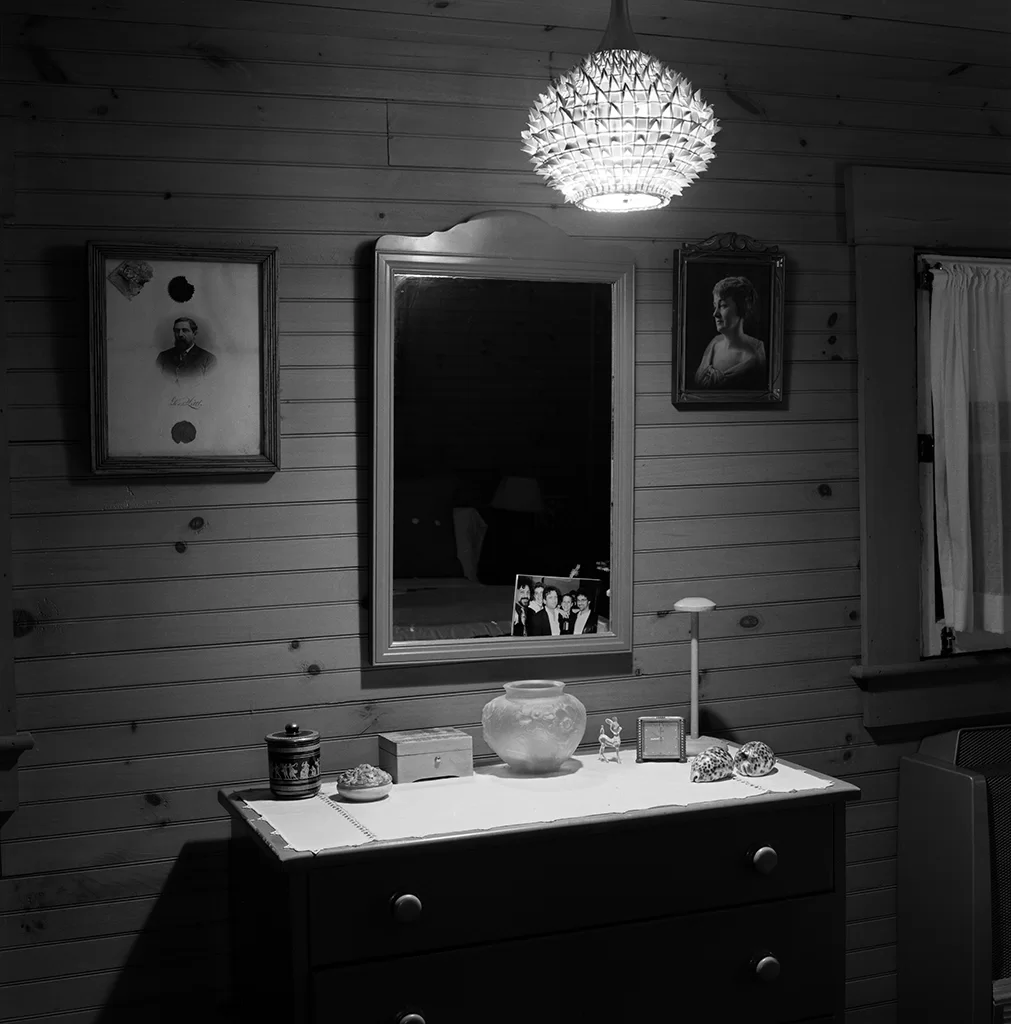 A bathroom vanity photographed in black and white beneath a lit chandelier.