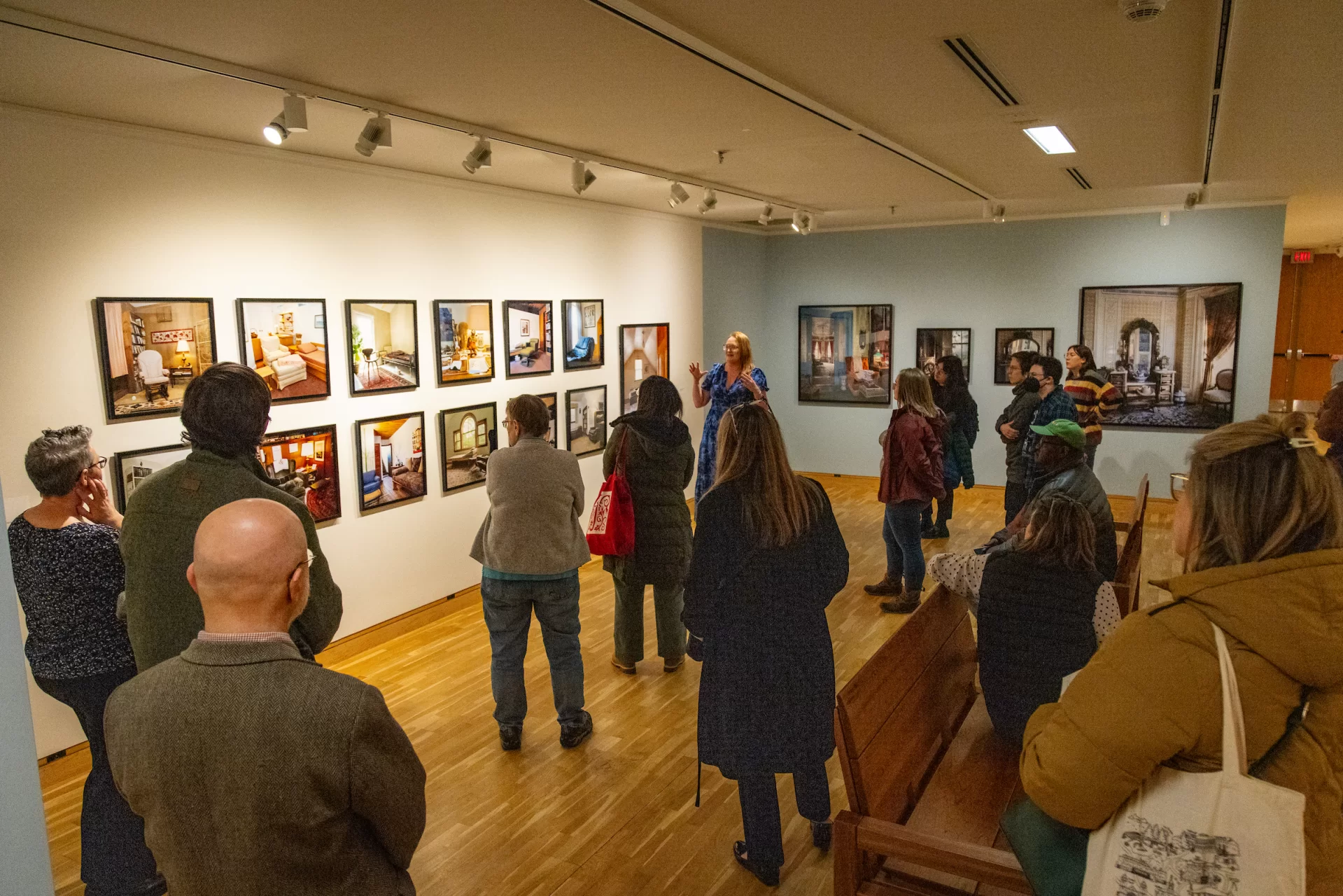 A person addresses a group of people in an art gallery filled with photographs.