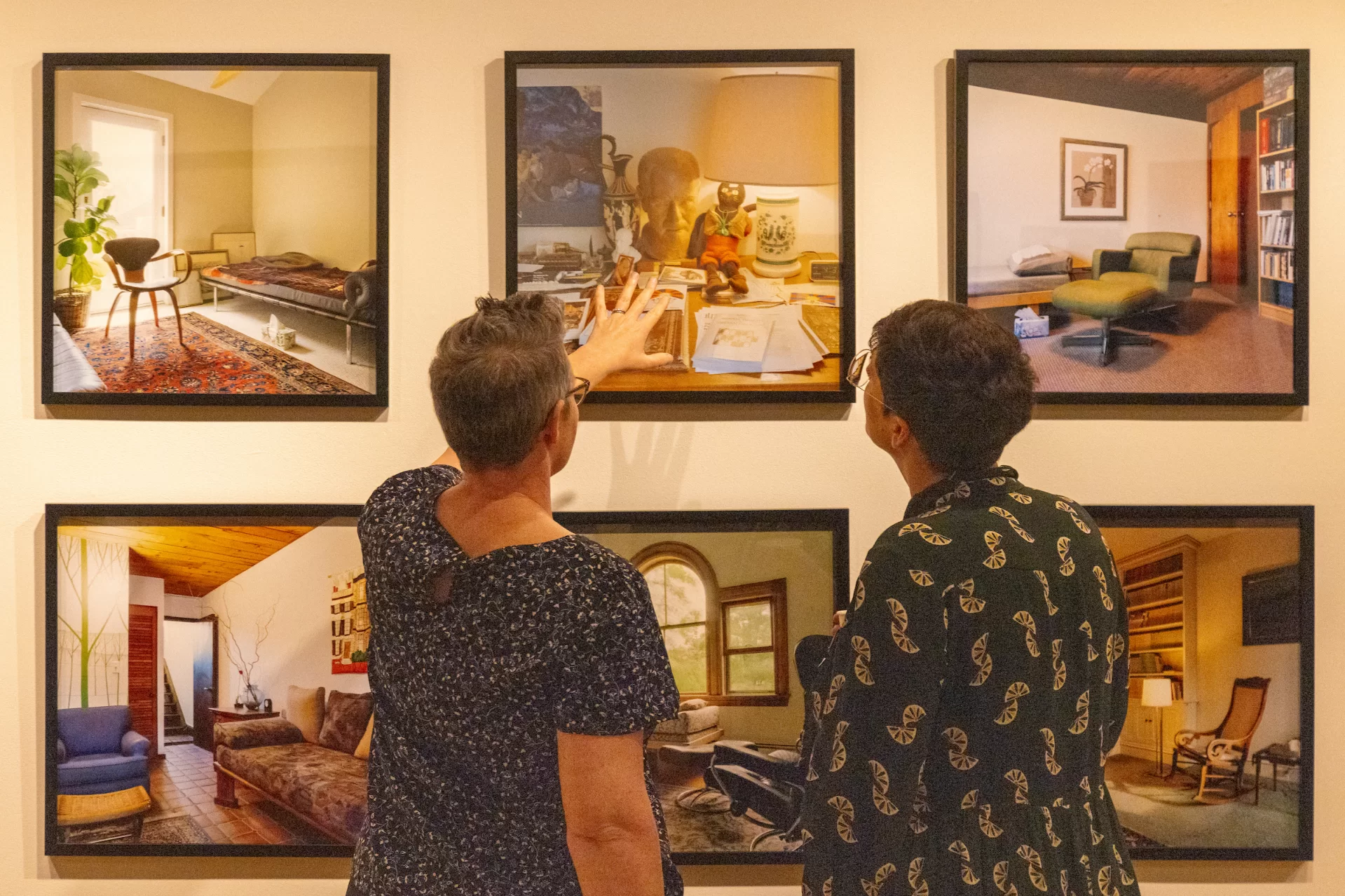 Two people gaze and point at photographs in an art gallery.