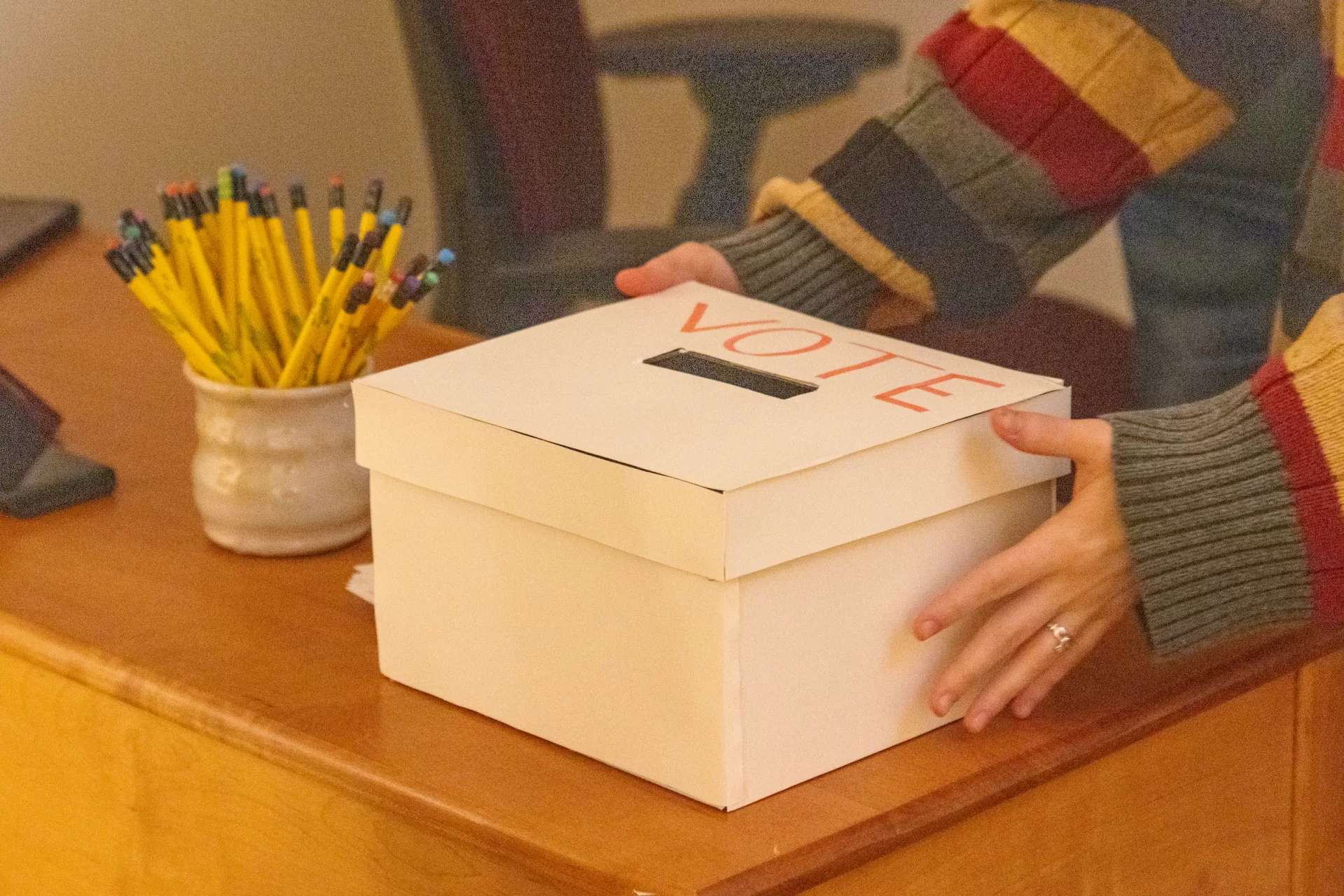 A person sets a voting box down on a desk.