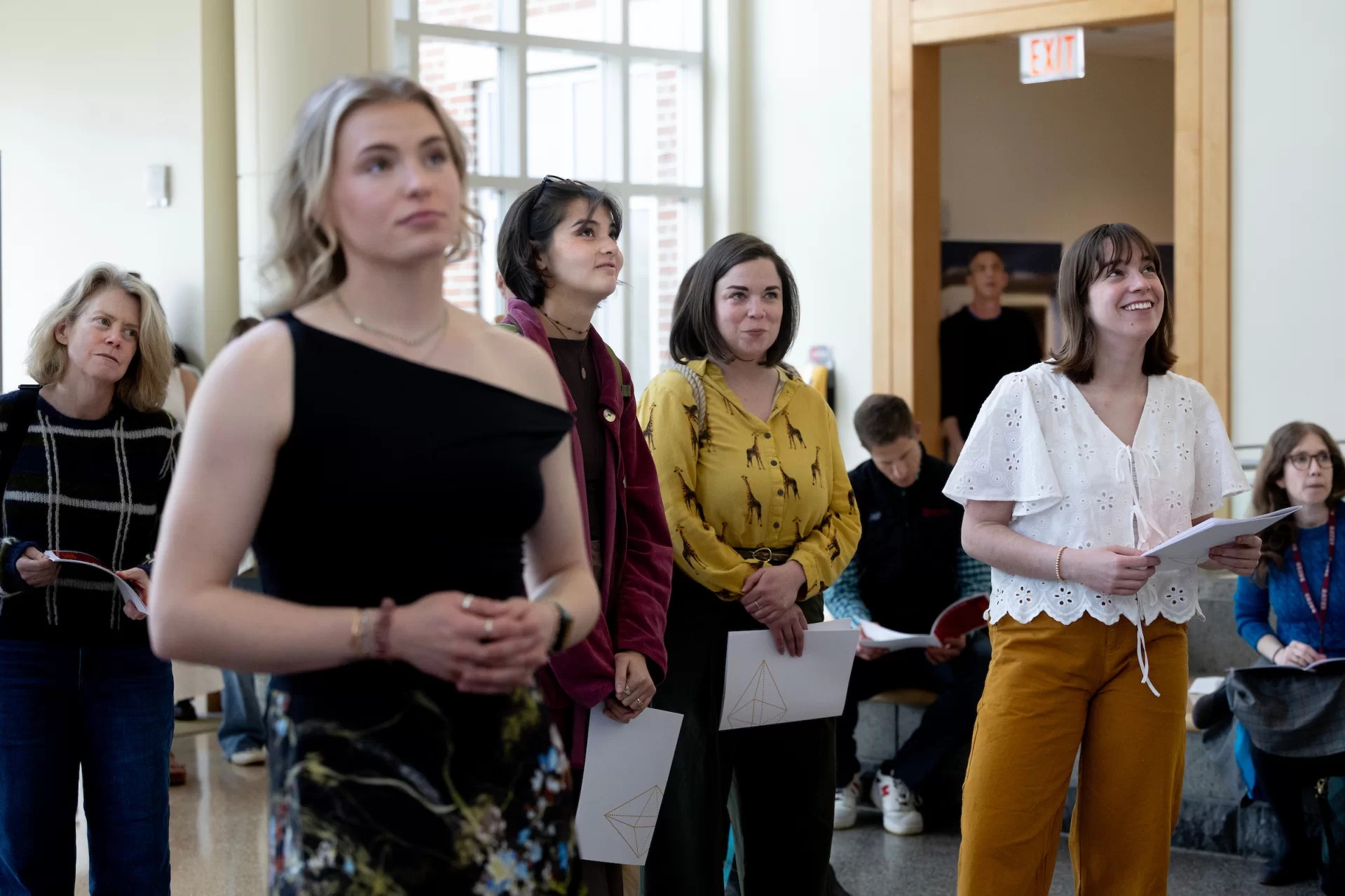 Women standing in an atrium listening to a speech.