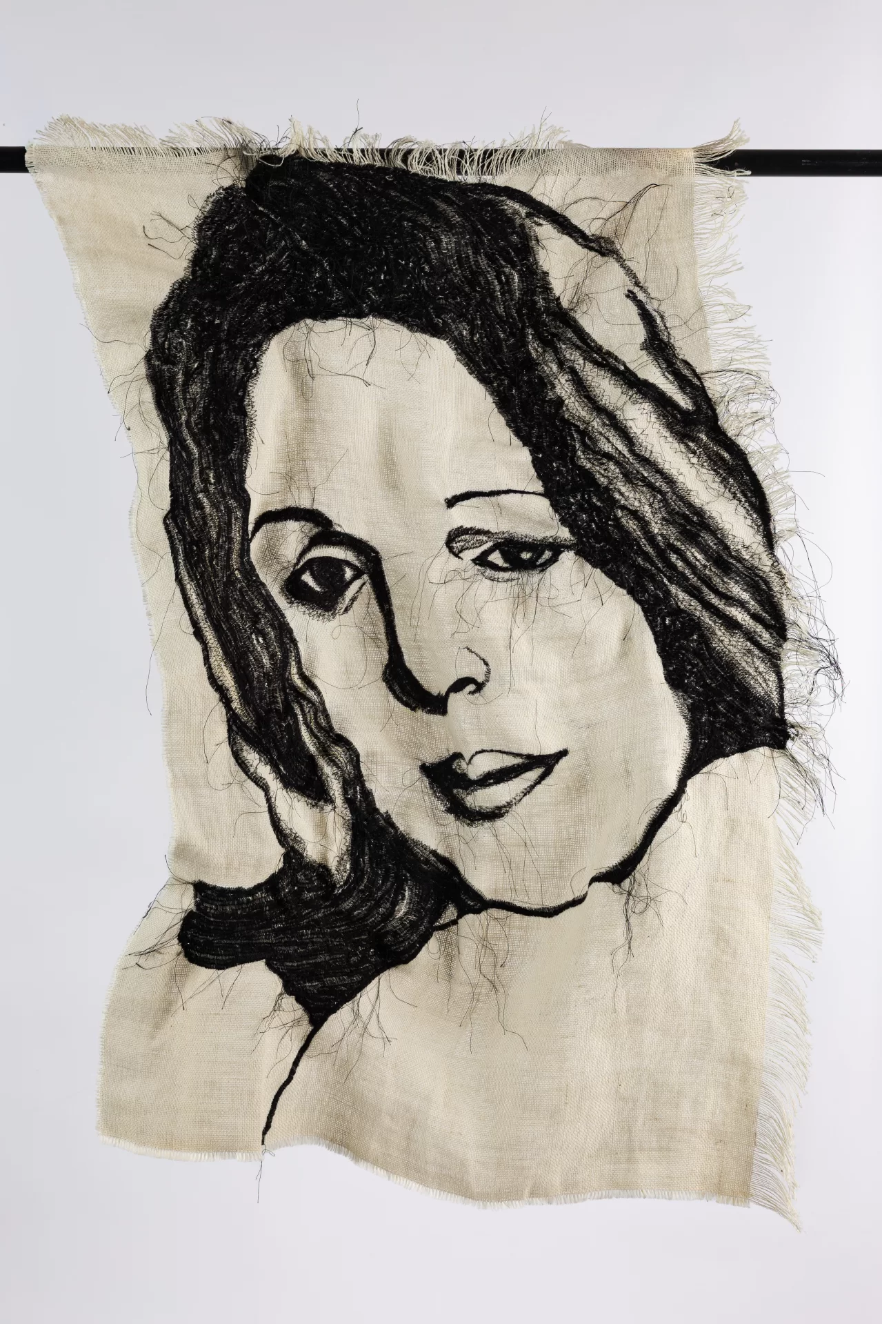 Embroidery of a woman's face on a beige tapestry.