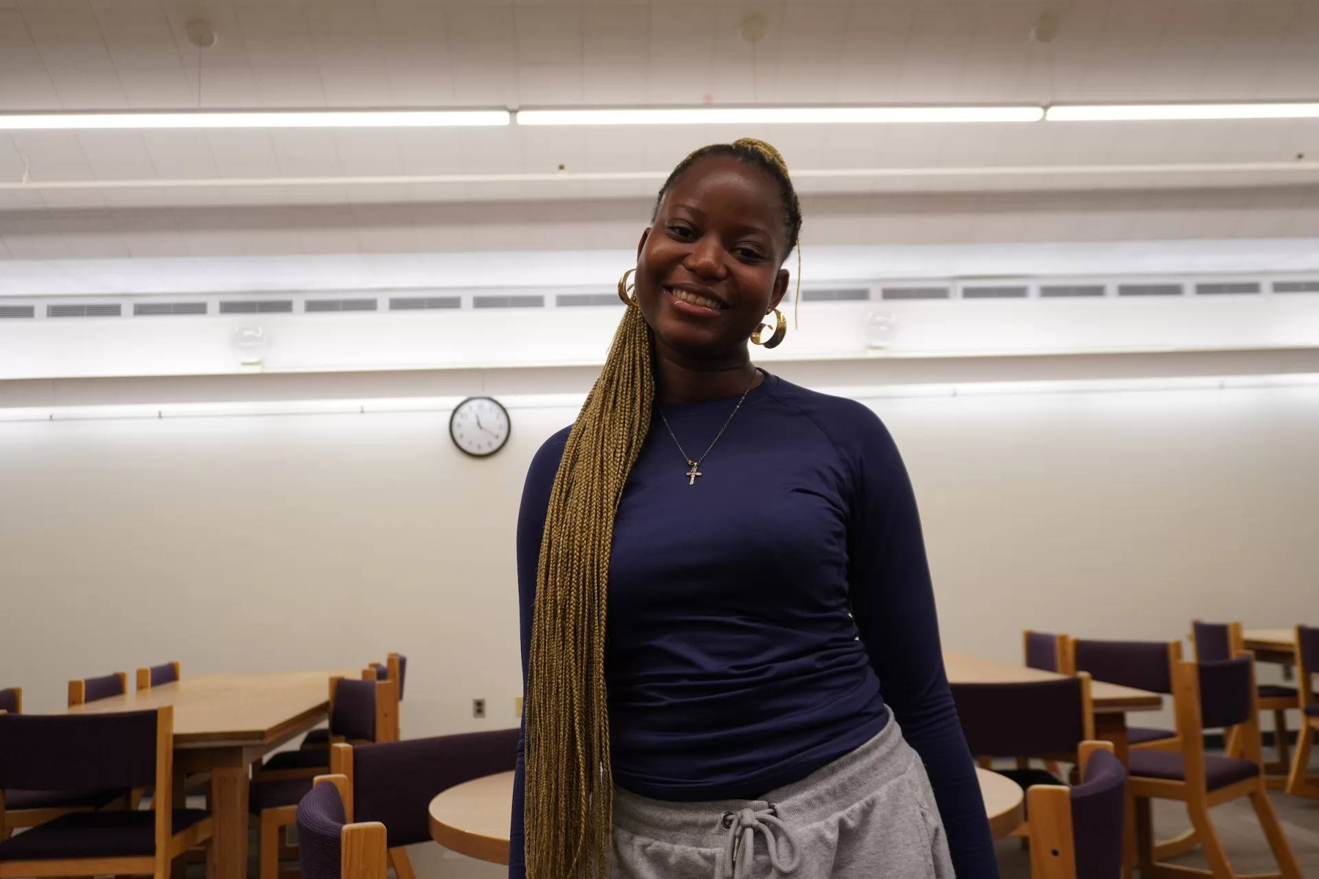 A woman smiling in a room with tables and chairs behind her.