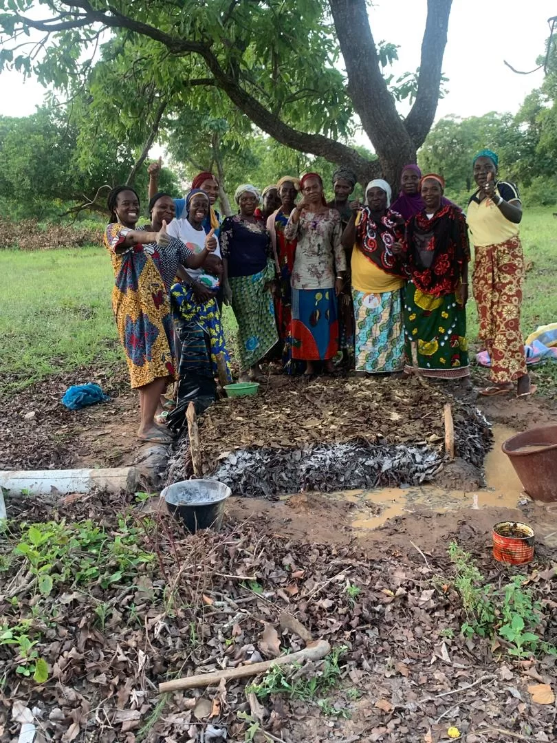 A group of woman in bright clothing stand together under a tree.