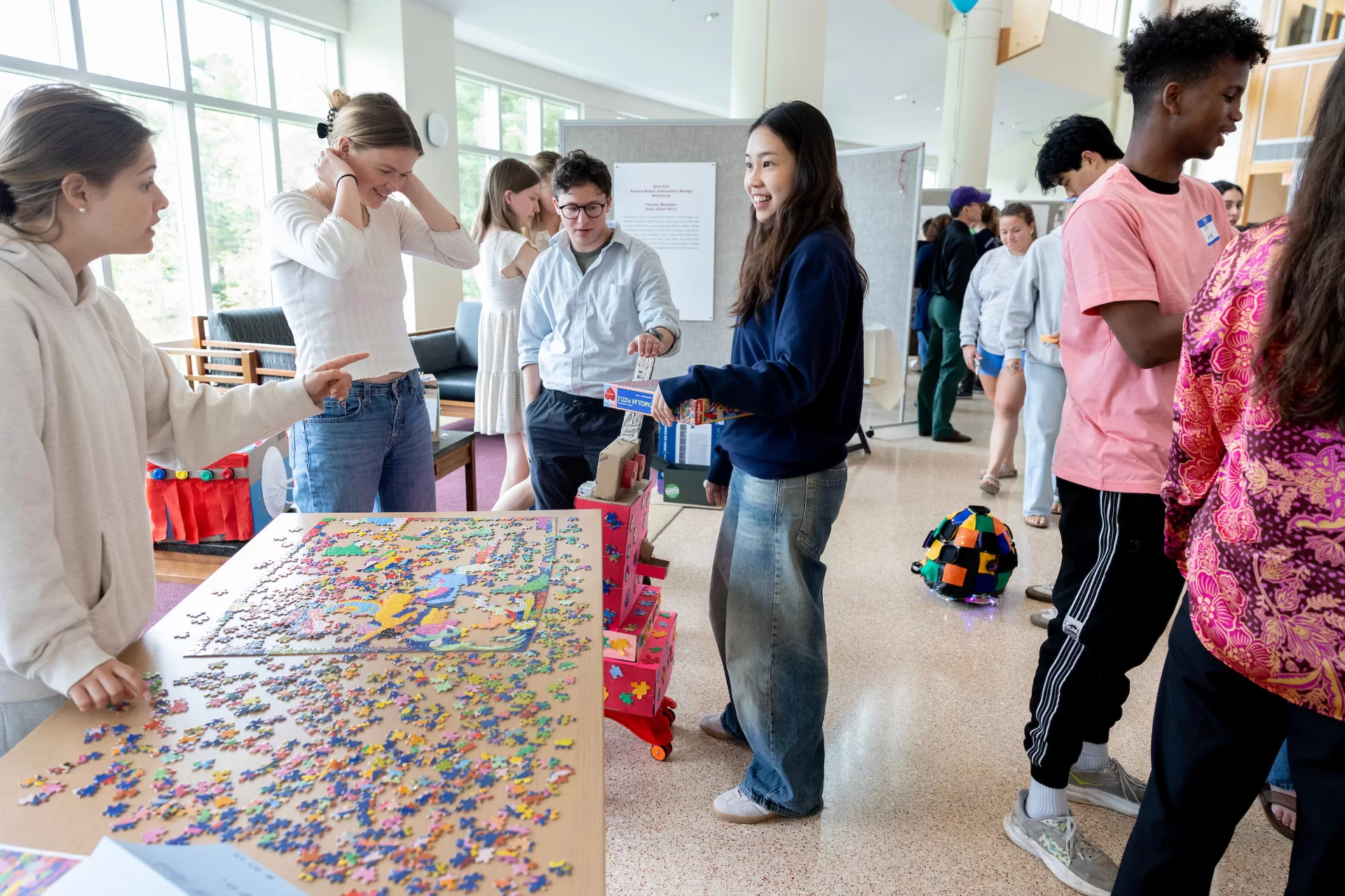 A group of people gather around a table with puzzle pieces atop in a presentation hall.