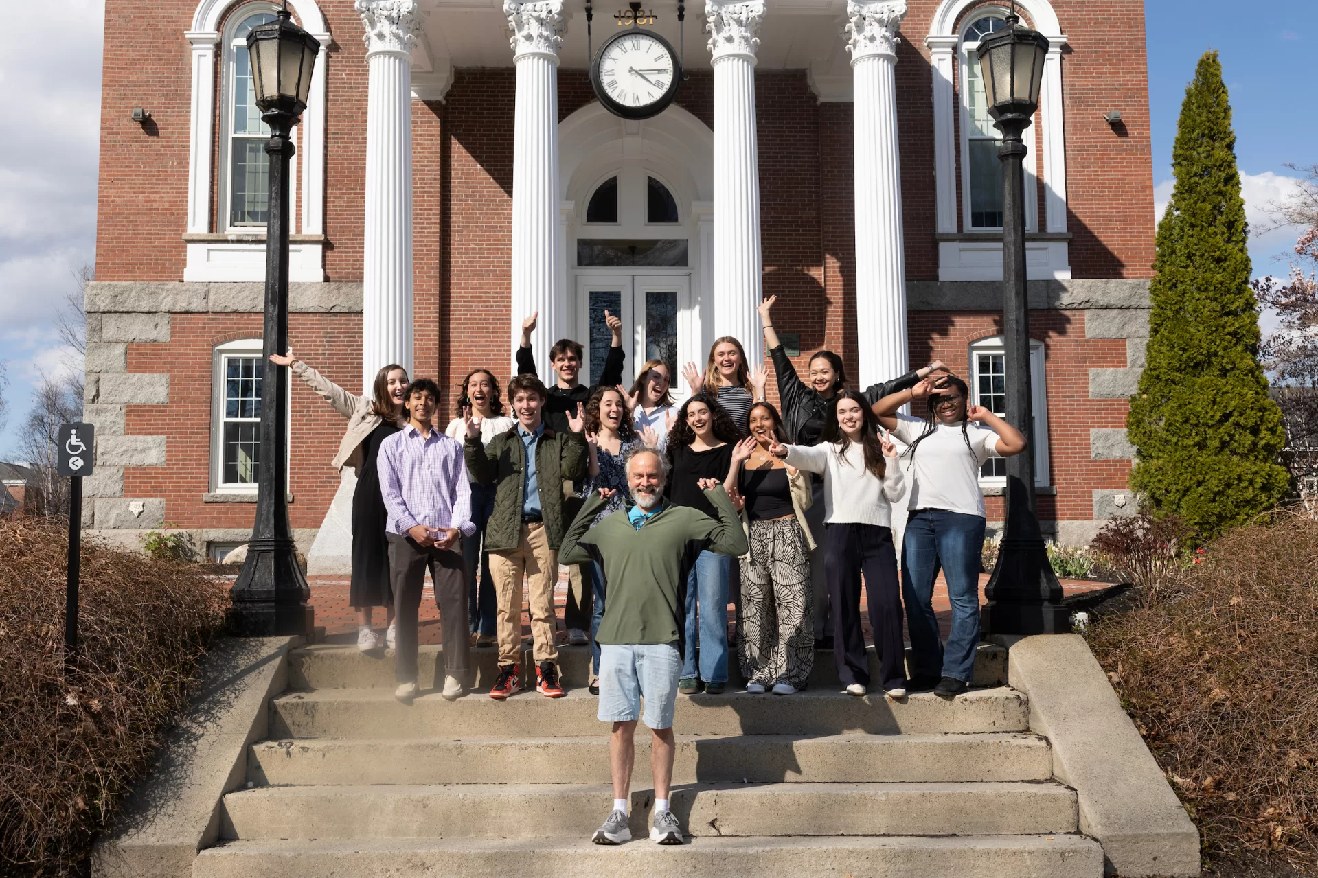 A group of people pose jubilantly on the steps of a building.