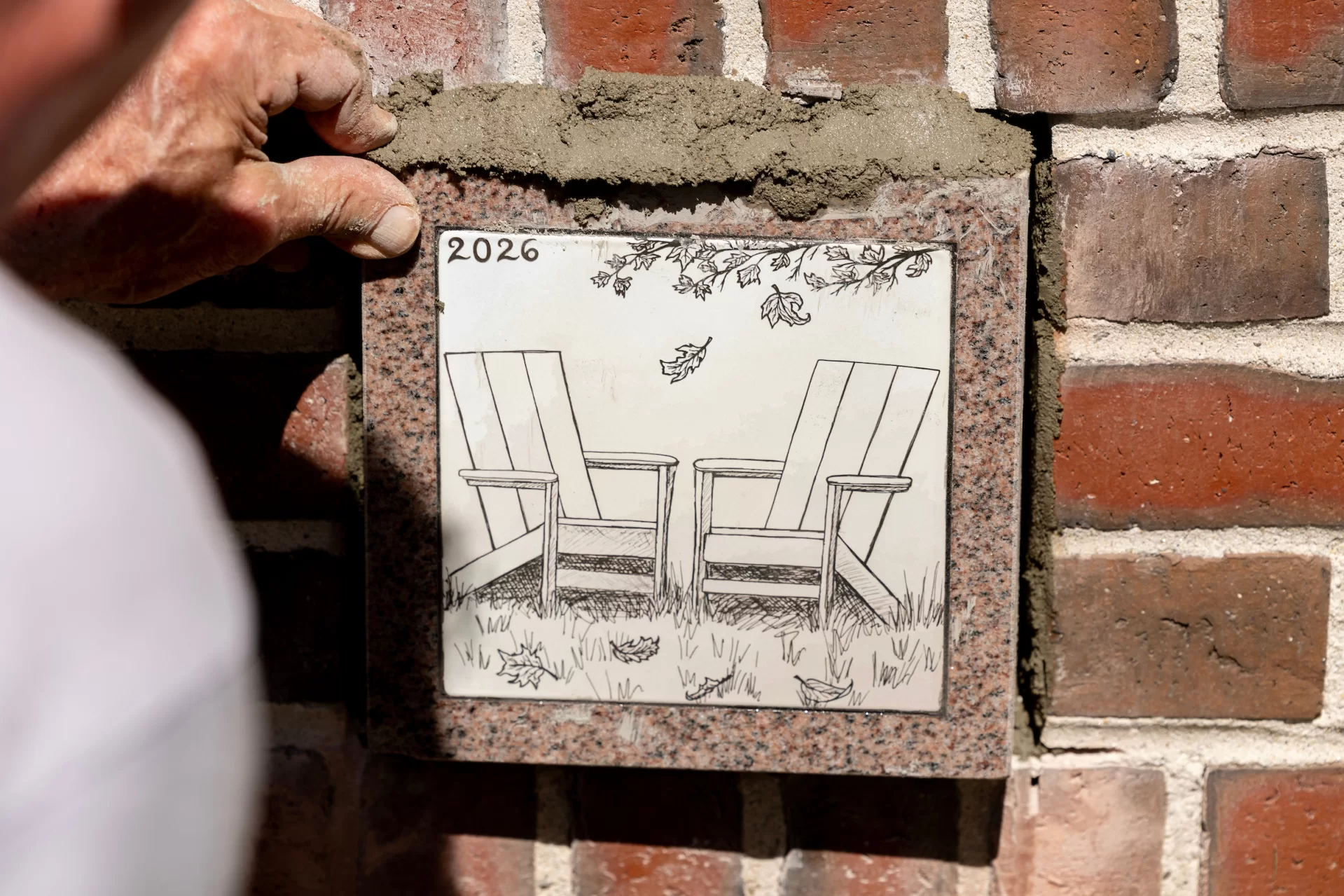 A hand pushing a decorative stone lined with spackle into a brick wall of a building.