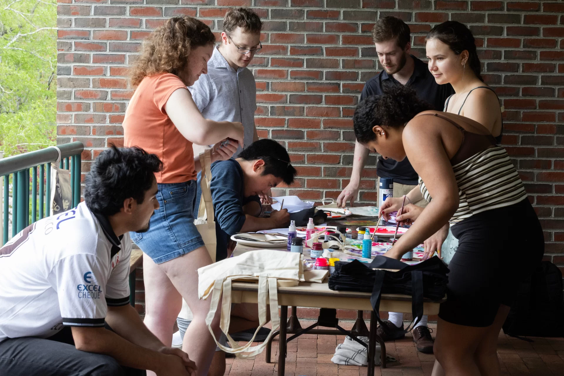 Students huddled around a table paint tote bags