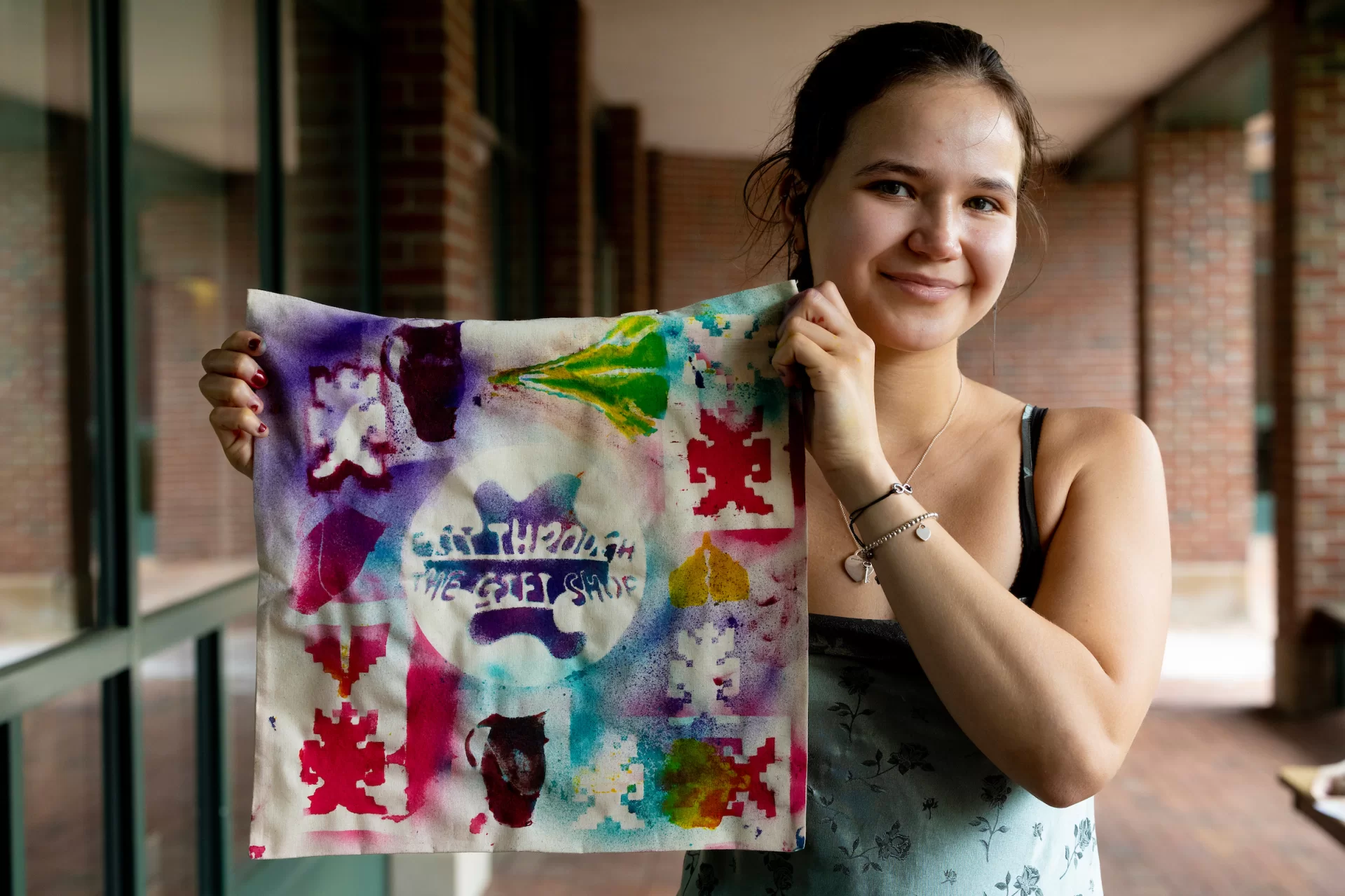 A student holds up a colorful spray painted tote bag