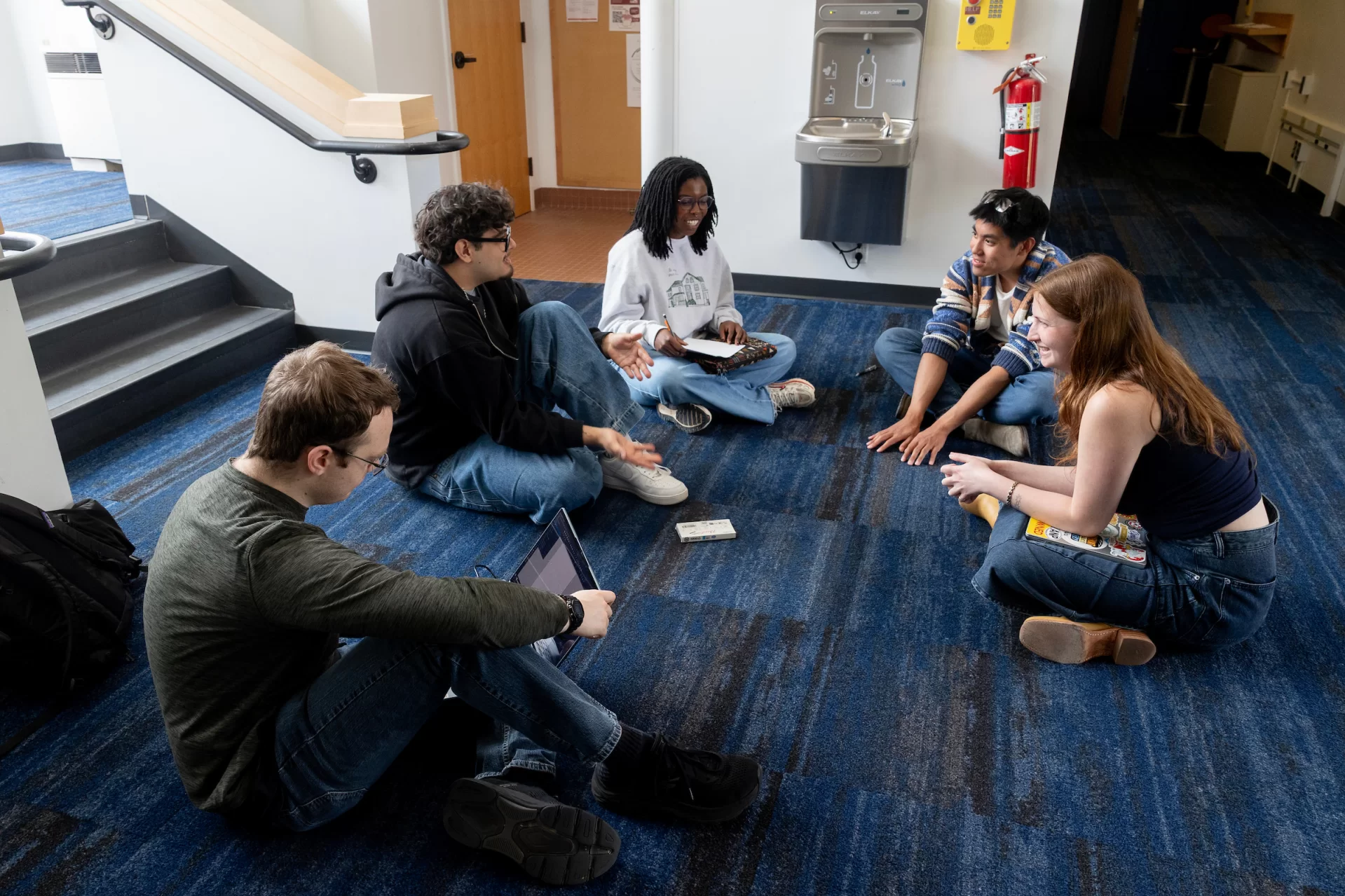 Students sit in a circle on a carpeted floor and chat