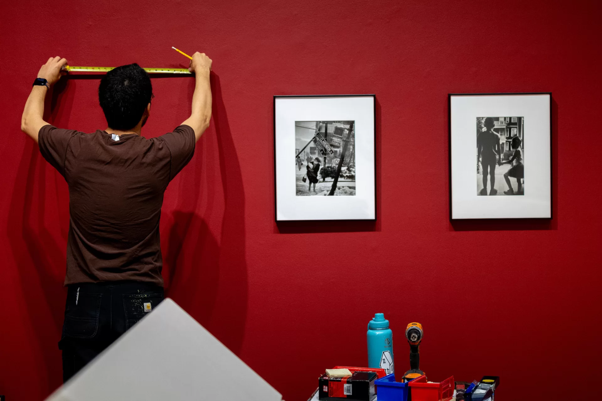 Installation of “Phyllis Graber Jensen: Picture Stories” in Bates Museum of Art with Kenny Rosen (in brown t-shirt) and Kevin Callalhan (black t-shirt) hanging framed photographs and with Museum Director Carrie Cushman with Multimedia Producer Theophil Syslo in front of title wall, on June 10, 2026.